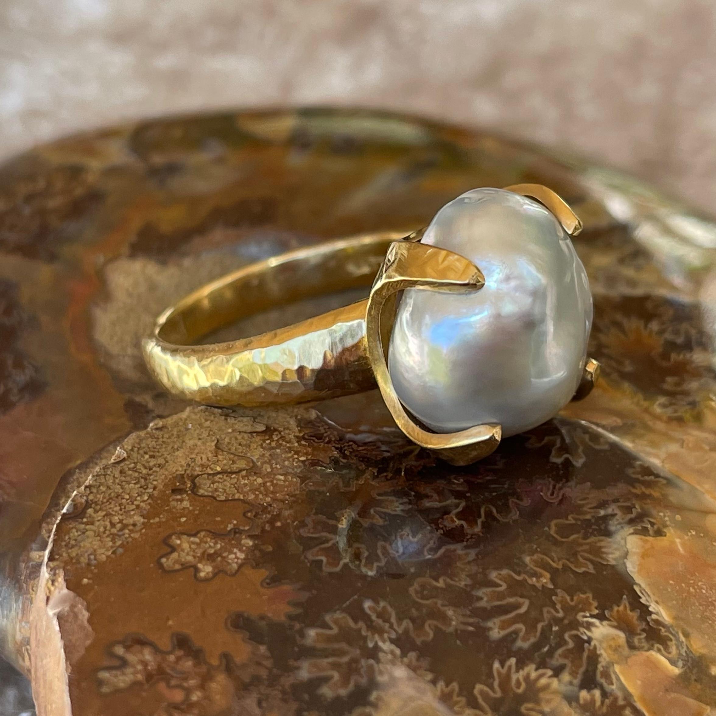 A beautiful approximately 13 mm natural Keshi pearl is held in an organic 4 hammered prong embrace atop a substantial tapered matte-finish hammered 18 gold band in this Steven Battelle design.  This ring is currently sized 7, but is resizable. 