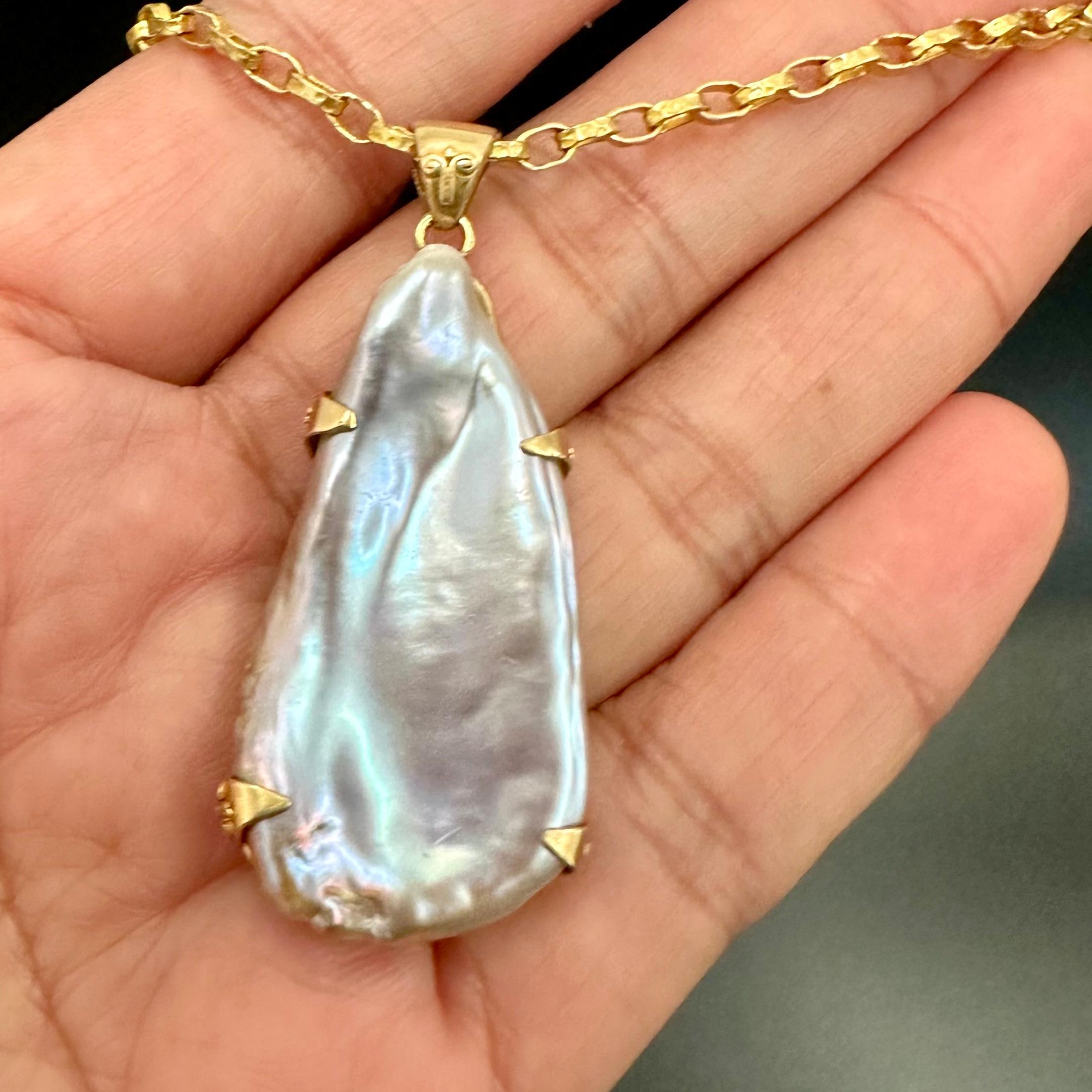 Una perla d'acqua dolce irregolare a forma di semi-perla di 20 x 40 mm, con varie sfumature di rosa e viola, è tenuta semplicemente in una montatura in oro 18 carati lavorata artigianalmente da quattro rebbi triangolari accentati da un piccolo
