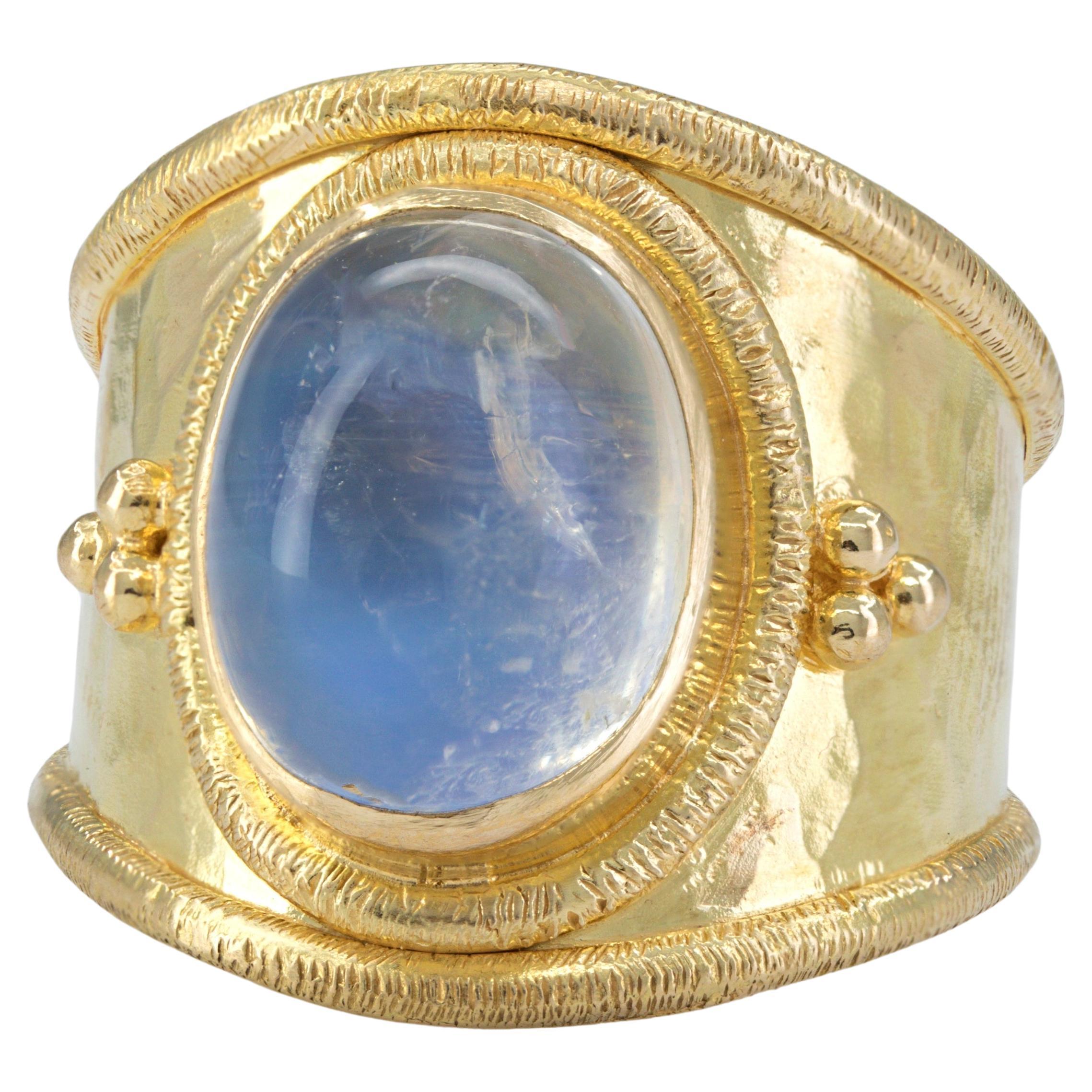 Featuring (1) oval rainbow moonstone cabochon, 11 X 9 mm, bezel set, flanked by coarse granulation, in 18k yellow gold, 17.9 mm tapering to 5.9 mm, size 6.75, marked BATTLLE 18K, Gross weight 7.16 grams.