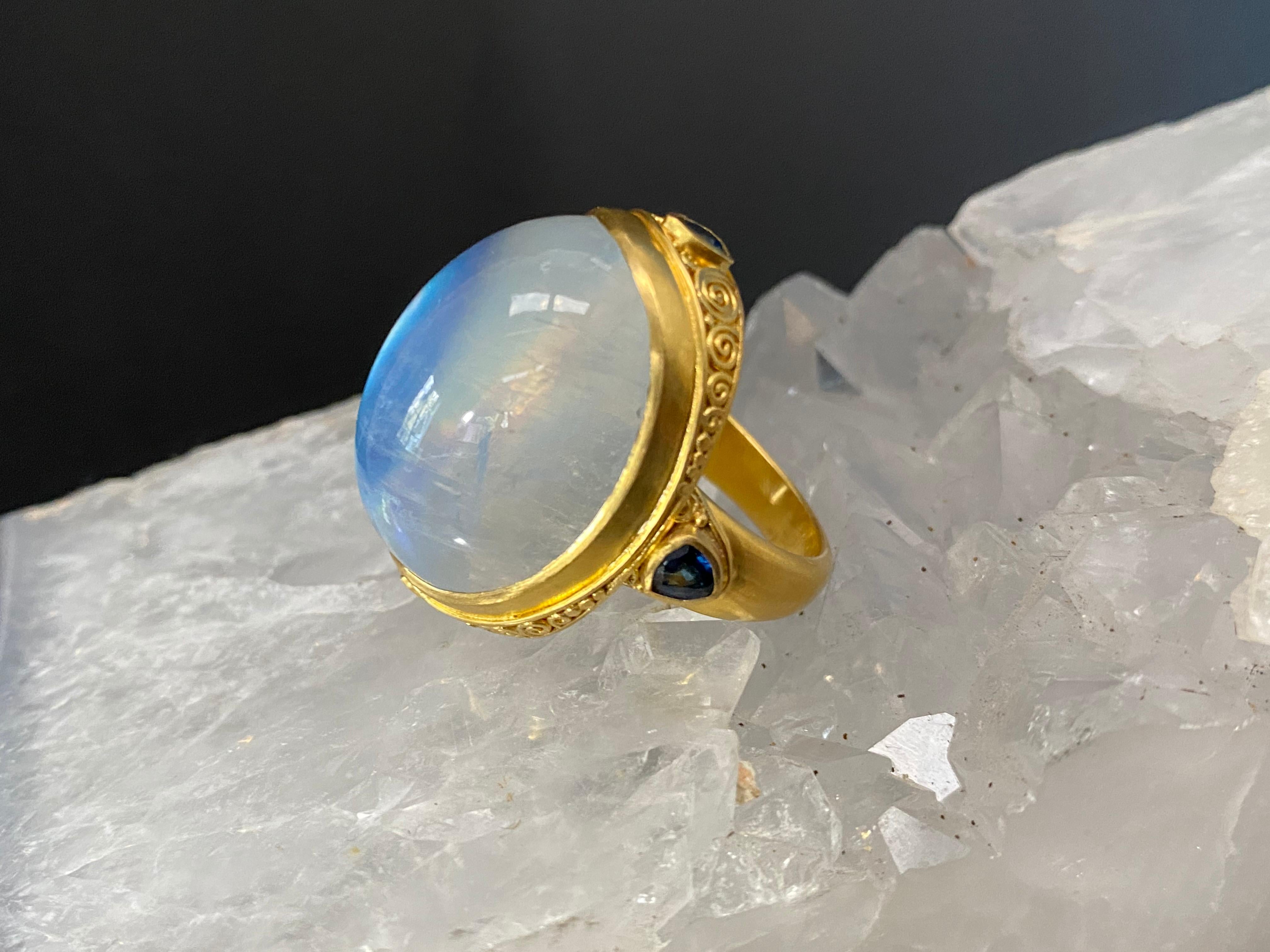 A signature classic Steven Battelle cocktail ring with a huge 19 x 24 mm shimmering oval rainbow blue moonstone cabochon and a carat of trillium faceted blue sapphires set in a handmade ancient-inspired 