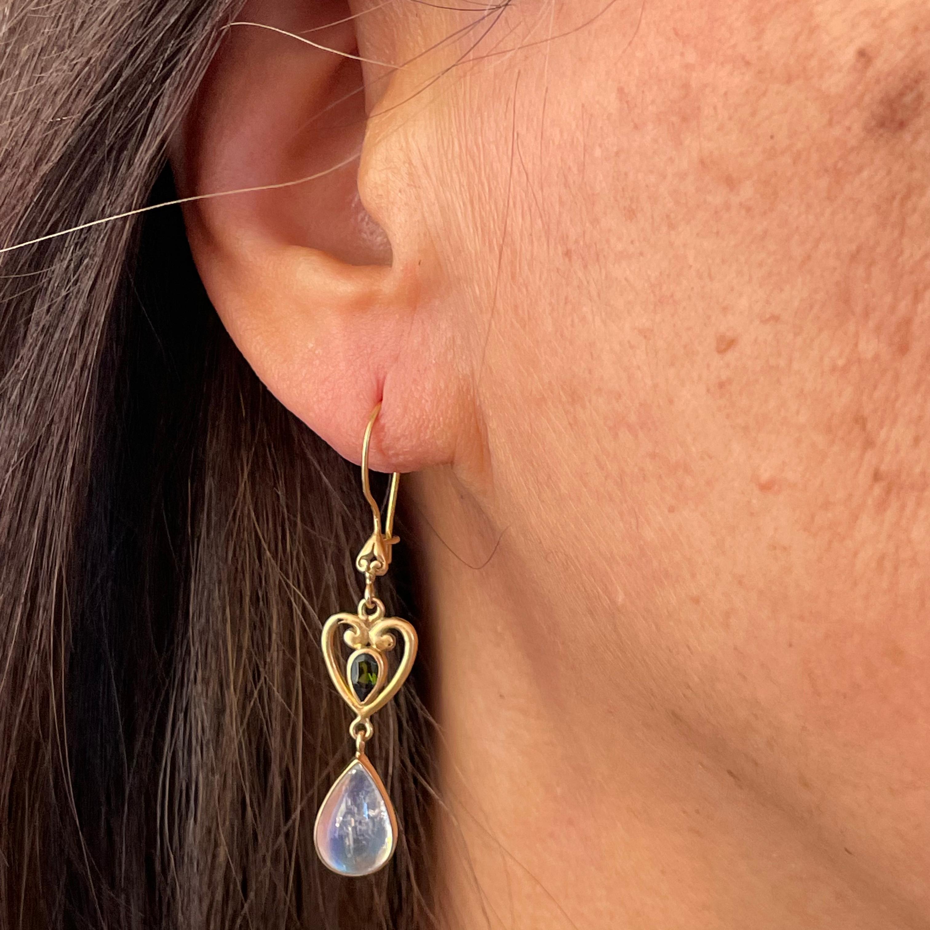 Two shimmering 8 x 12 mm rainbow moonstone pear shaped drops totaling 5 carats are suspended below heart shaped gold components with central small 3 x5 mm faceted green tourmalines in this Steven Battelle design. Safety clasp wires. 
