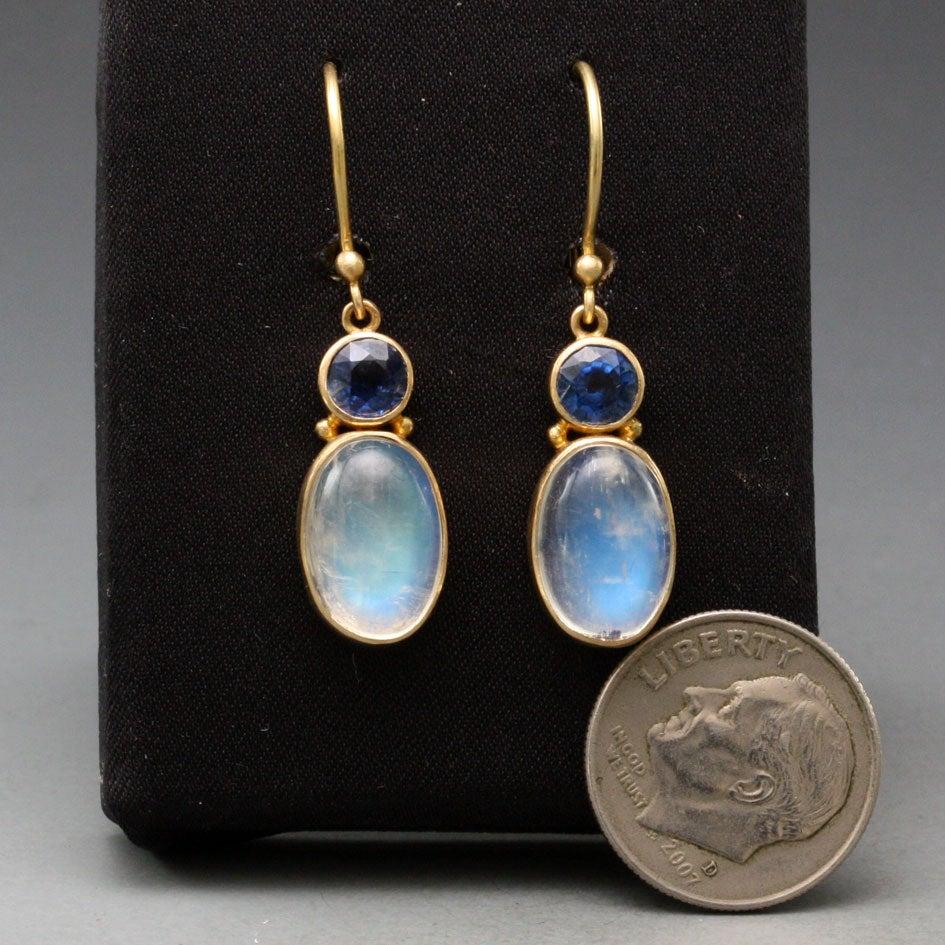 Long oval 8x11 mm Rainbow Moonstone cabochons are set below 5 mm faceted 18K faceted deep blue Kyanites in this beautifully complementary Steven Battelle design.  
11.1 carats stone total.  Safety clasp wires.

