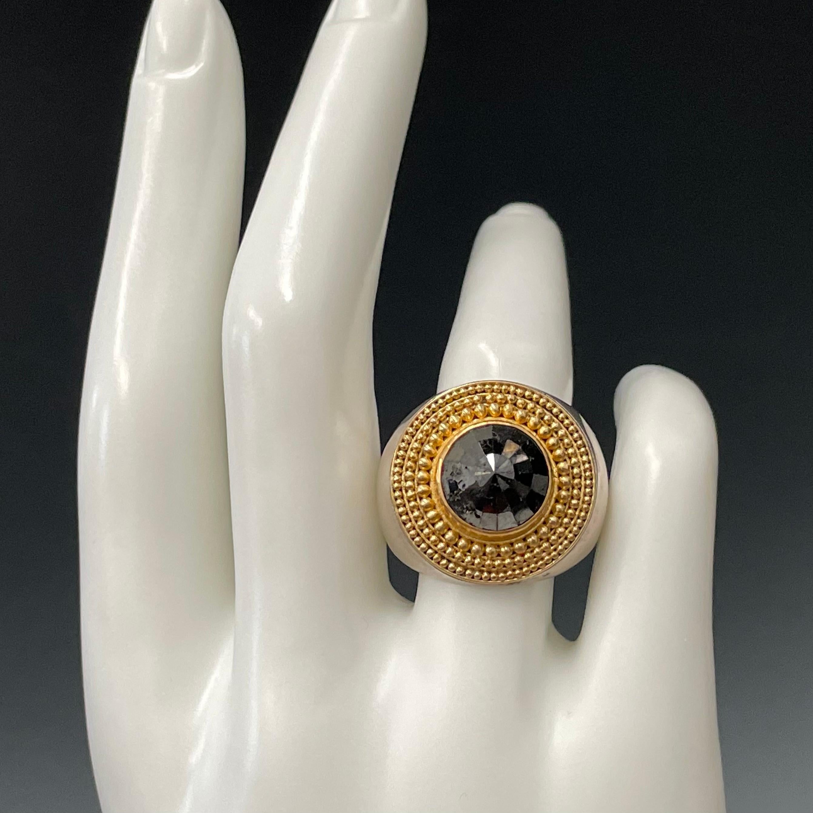 A 10 mm 7.3 Ct rose cut domed black diamond is surrounded by radiating large to small 