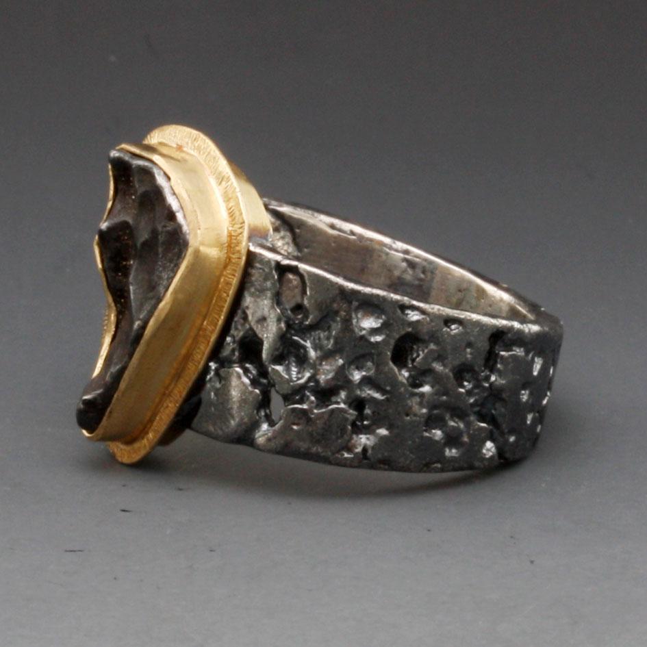Ein einzelnes, unregelmäßiges, dreieckiges 8 x 13 mm großes Fragment eines Sinkote-Alin-Meteoriten, das von seinem flammenden Eintritt in die Atmosphäre mit einer Schmelzkruste übersät ist, wird in eine handwerklich gefertigte Lünette aus