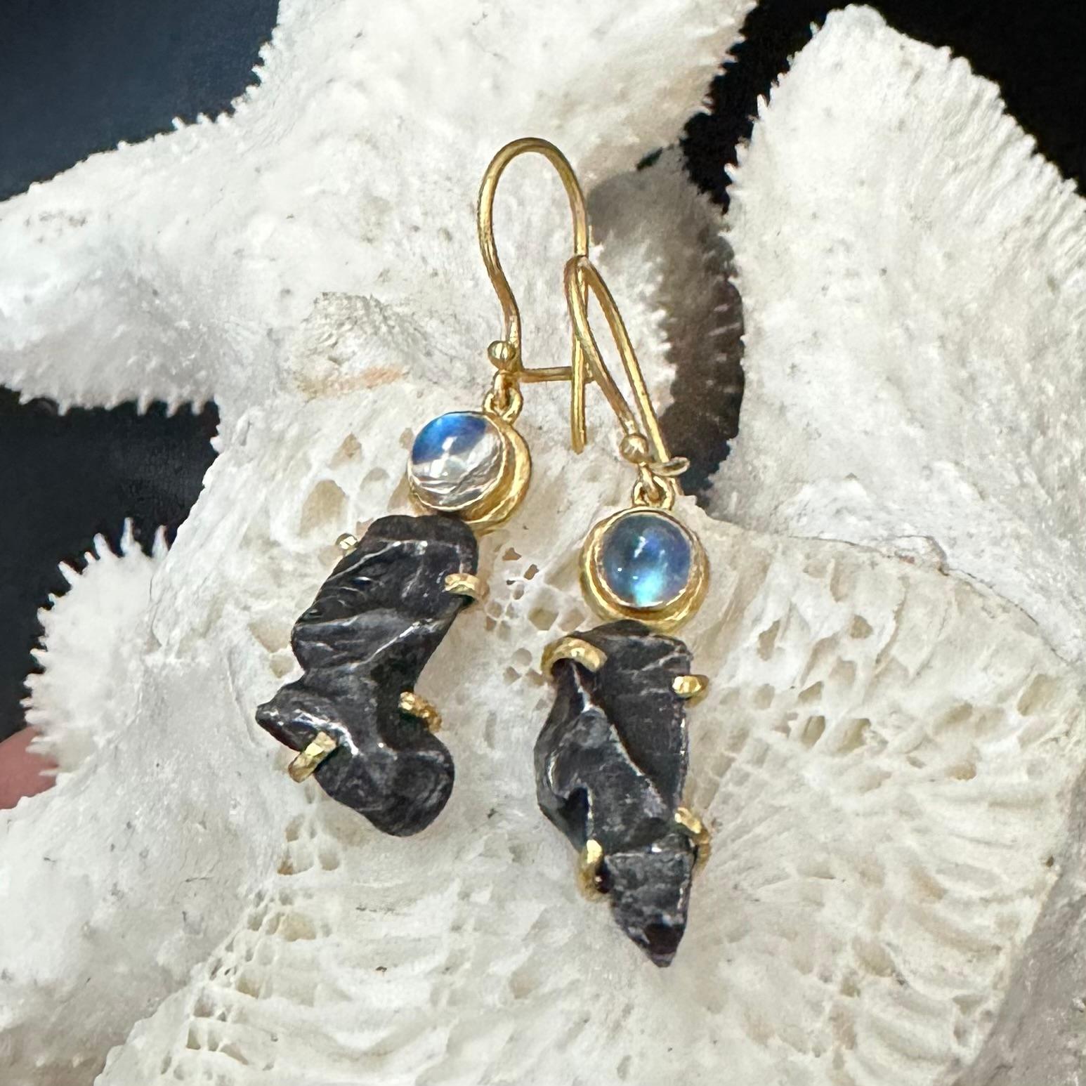 Due frammenti irregolari e incisi dalla fiamma del meteorite Sinkote-Alin sono trattenuti da punte in oro 18K sotto un paio di pietre lunari blu lampeggianti di 6 mm in questo orecchino dal design 