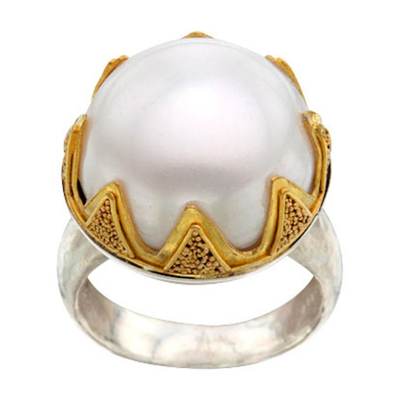 A 17 mm lustrous white Mabe pearl is embraced by eight 22K bezel prongs decorated with fine 