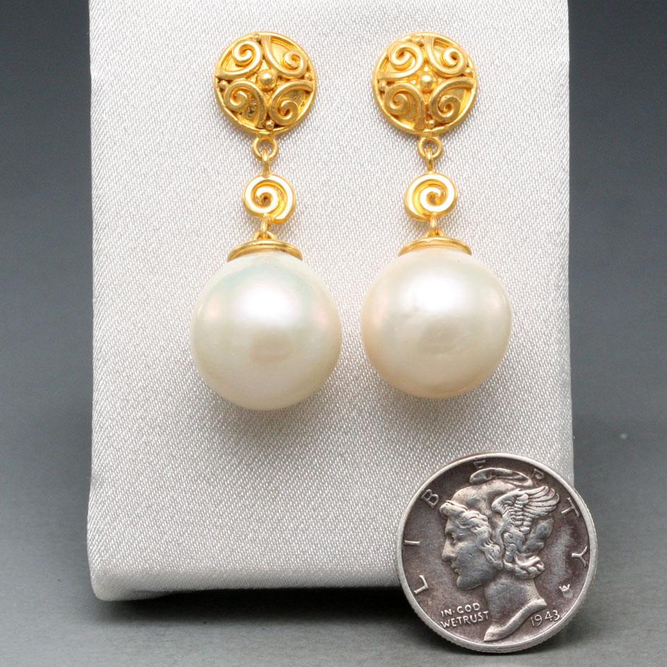 Two lustrous 14mm fresh water drop pearls are suspended below handmade slightly domed 18K posts decorated with heavy wire spirals and a single central 