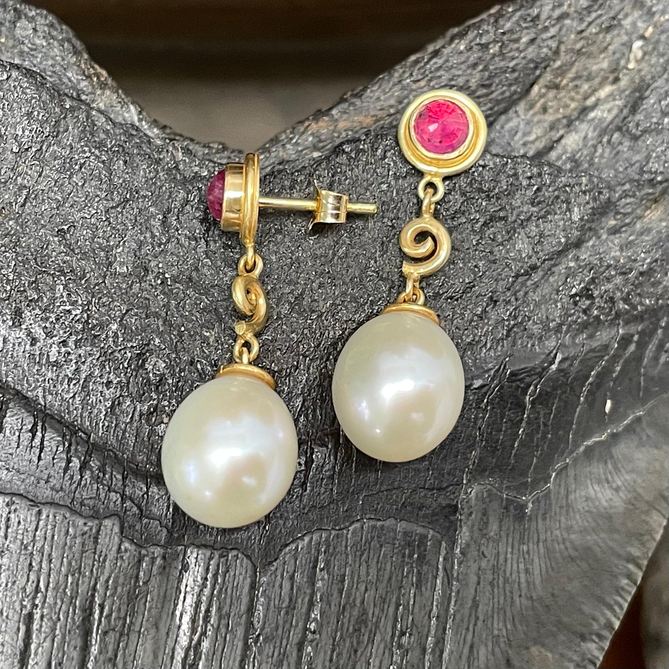 Two lustrous 12 mm drop freshwater pearls are suspended below 4mm reverse faceted rubies (1.2 carats total) posts, with spiral accent components between, in this opulent creation.  The color contrasts between ruby, gold and pearl enchant.  