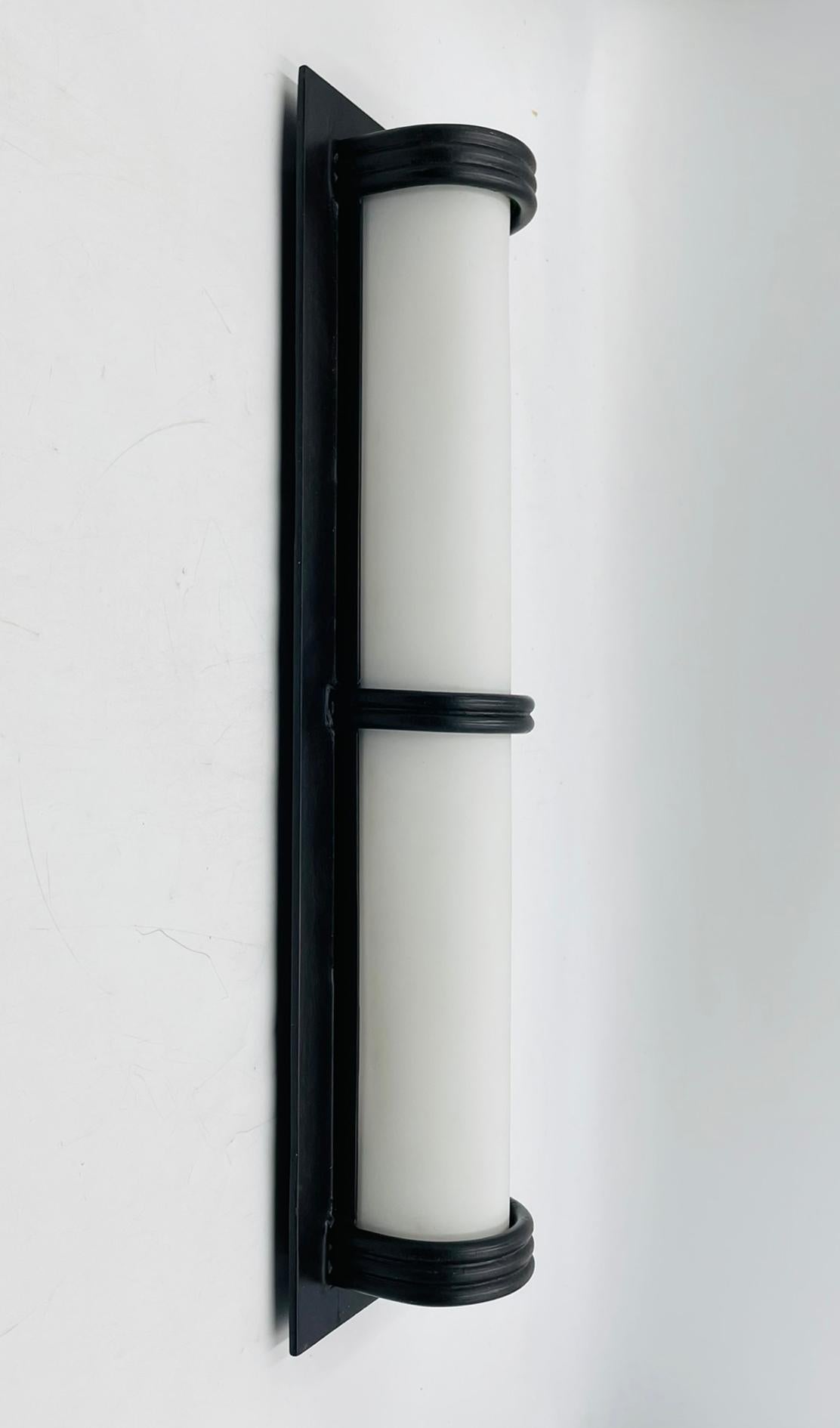 Un'unica applique scultorea realizzata a mano da Steven Handelman Studio a Santa Barbara, California. Questo pezzo è caratterizzato da un diffusore cilindrico in acrilico bianco racchiuso in una struttura minimalista in ferro battuto nero, che offre