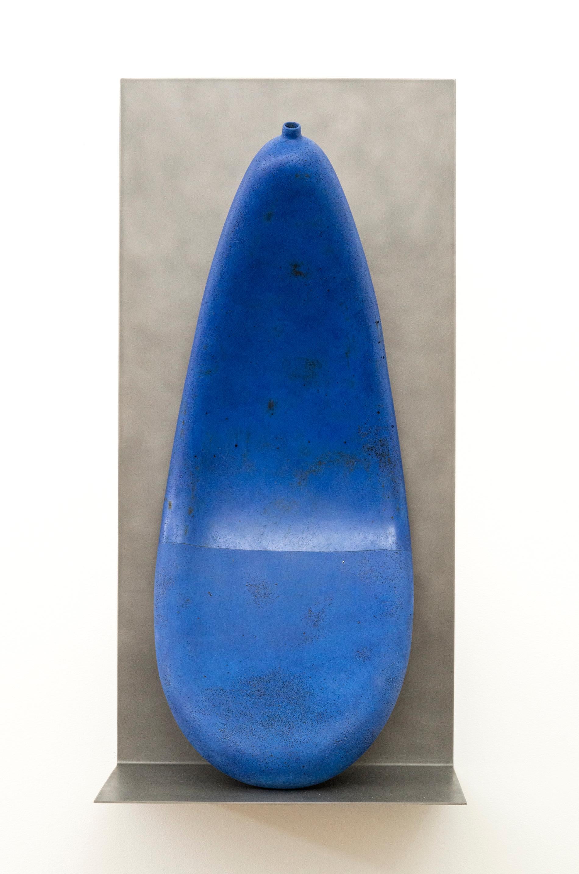 Diese faszinierende große blaue Tonarbeit des kanadischen Künstlers Steven Heinemann überbrückt die Kluft zwischen Skulptur und Keramik. Das tropfenförmige Gefäß wirkt entleert und sanft gekrümmt, als ob es das Stahlregal, auf dem es steht,