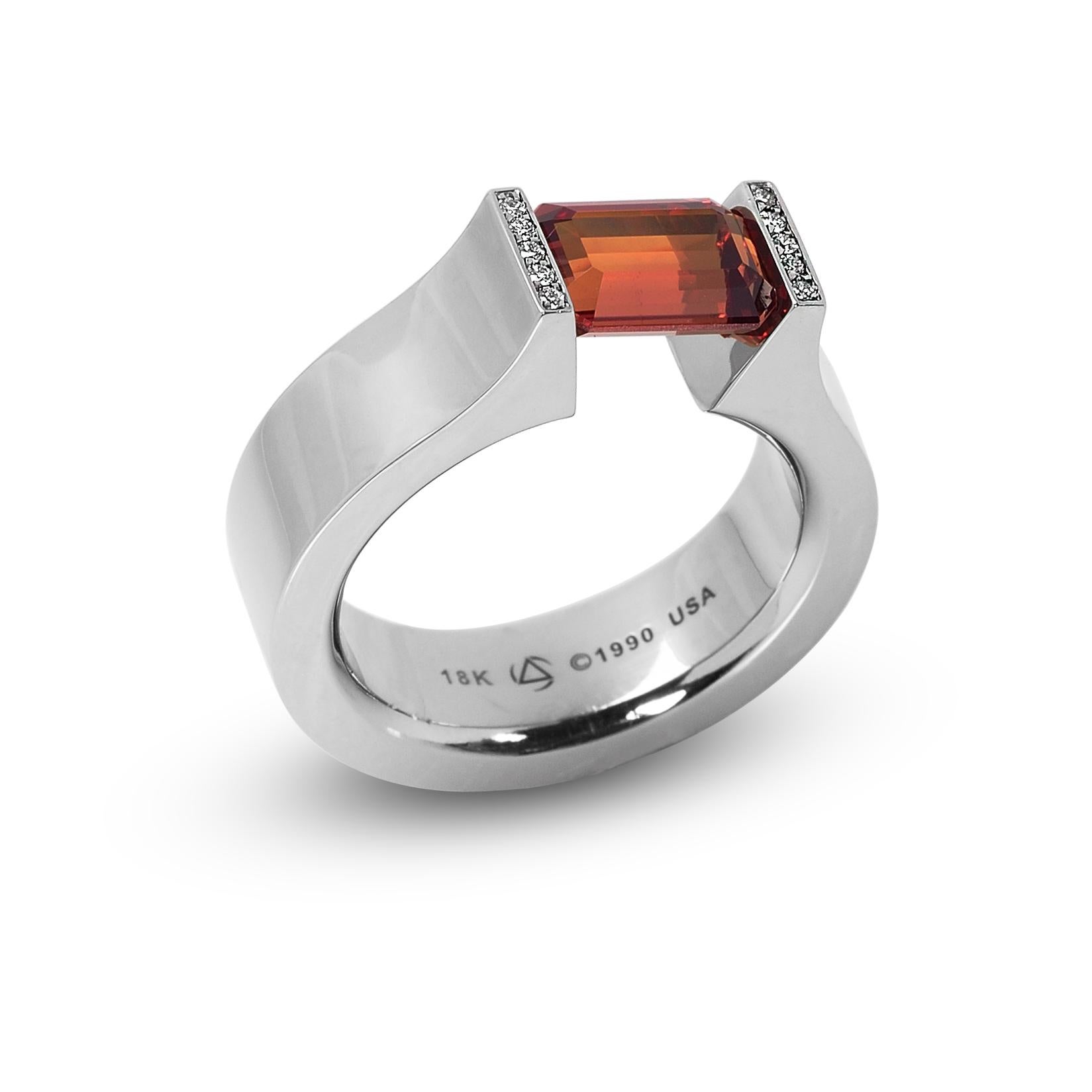 The Steven Kretchmer Hard Omega ring with pave lips and a tension-set orange sapphire is handcrafted in 18K white gold with a shiny finish. The 2.27 ct. emerald cut sapphire is a deep and fiery citrusy orange. The setting features five F/VS diamond