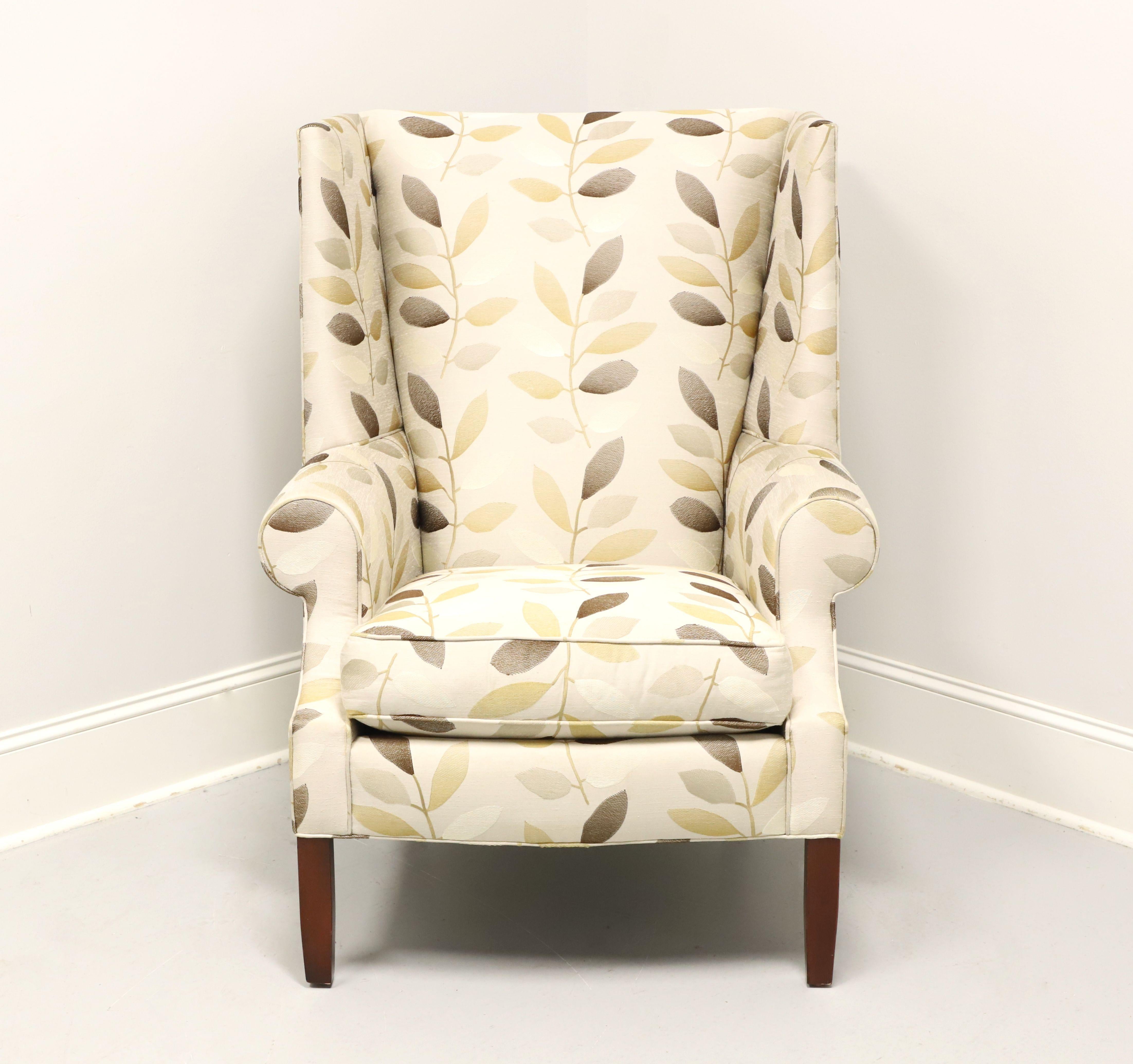 A Transitional style wing back chair by Stickley Furniture, their Park City. Fabric upholstered in a pattern of various neutral tone leaves amidst a beige color base on a cherry wood frame with their Metro finish to the tapered straight front legs