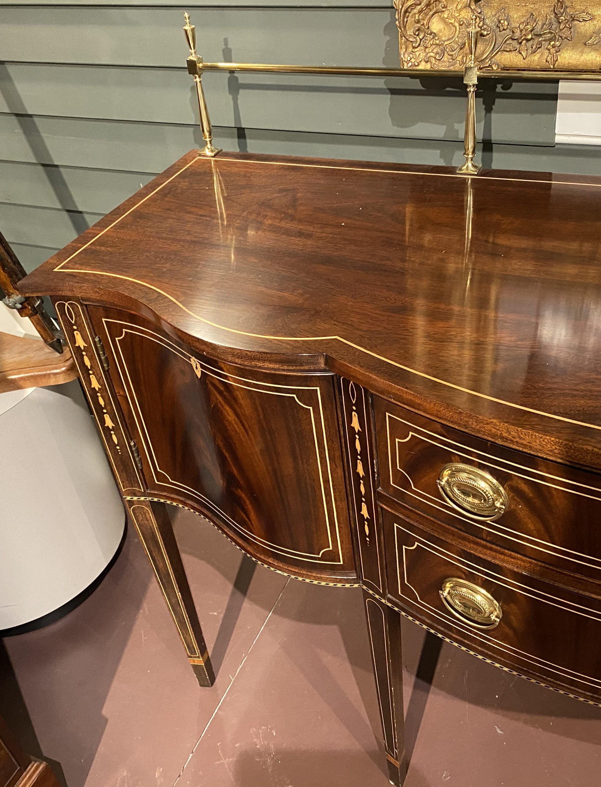 Credenza in mogano intarsiato in stile Feder di ottima fattura, con galleria in ottone sul piano sagomato con bordo intarsiato che sormonta una cassa con due cassetti centrali per posate ornati da tiretti ovali in ottone e affiancati da ante