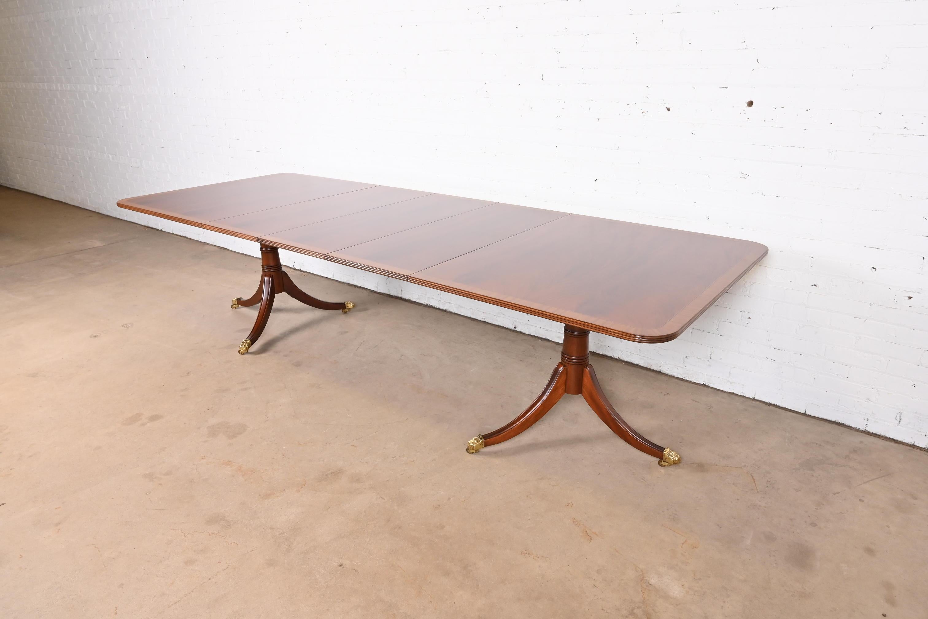 An exceptional Georgian or Regency style double pedestal extension dining table

By Stickley

USA, Late 20th Century

Beautiful flame mahogany top, with satinwood banding, carved solid mahogany pedestals, and brass paw feet on brass