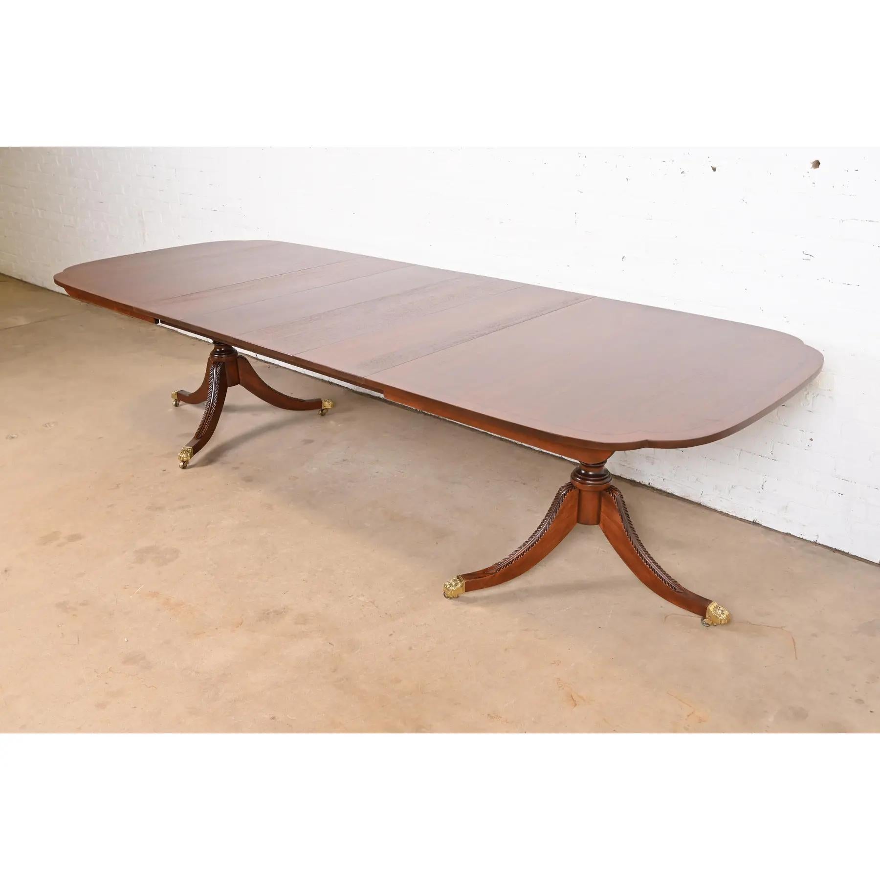 Exceptionnelle table à manger à rallonge à double piédestal de style Géorgien ou Régence.

Par Stickley

États-Unis, fin du 20e siècle

Magnifique plateau en acajou massif avec coins festonnés, incrustation de cordes en ébène, piédestaux sculptés et