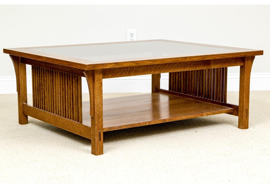 Stickley Mission Collection oak cocktail table with smokey glass insert, having a lower tier, open front and back with slatted side panels, exposed through tendons, shop mark medallion and burned-in Stickley logo and resting on square feet.
Model