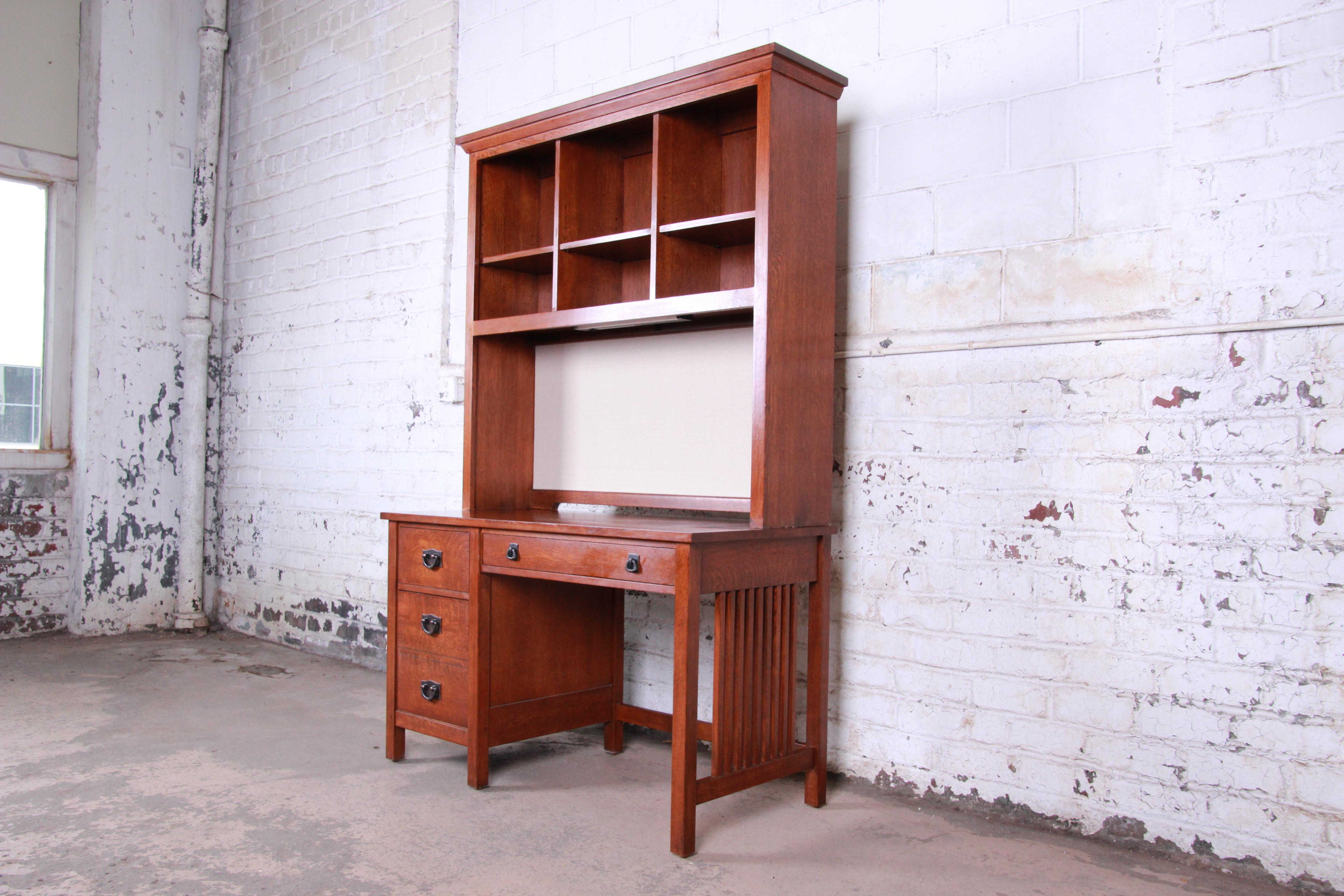 Vintage Mission oak desk by Stickley. The desk offers a lighted hutch top for storage and organization containing three sections with shelving. The desk has a large writing surface with a large drawer on the right portion and two drawers to the left