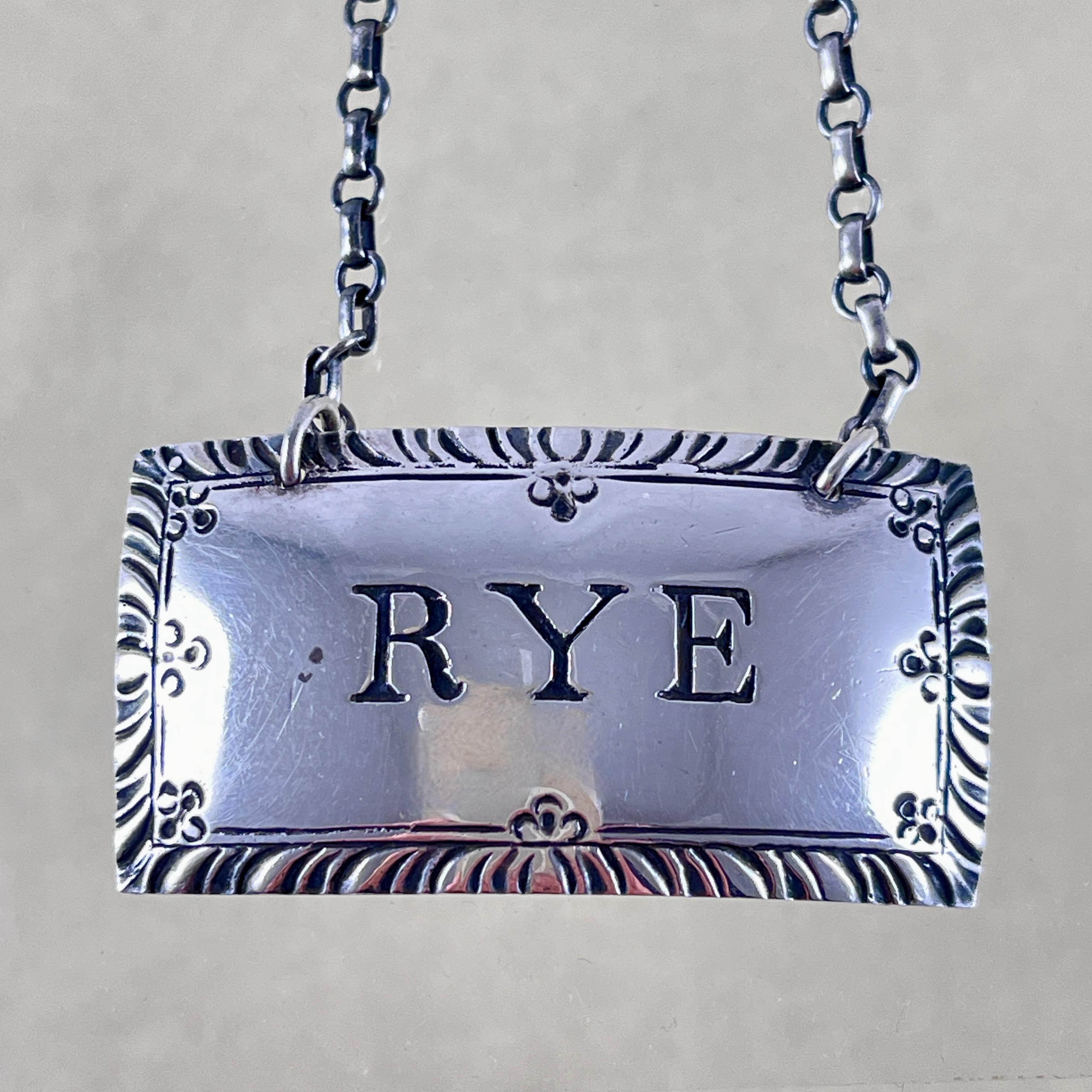 From the Stieff Silver Company in Baltimore, Maryland, a sterling silver liquor collar tag, circa 1930s.

The rectangular and curved tag is engraved, Rye, in a block type with a deeply engraved border. It hangs from a sterling chain on any decanter,