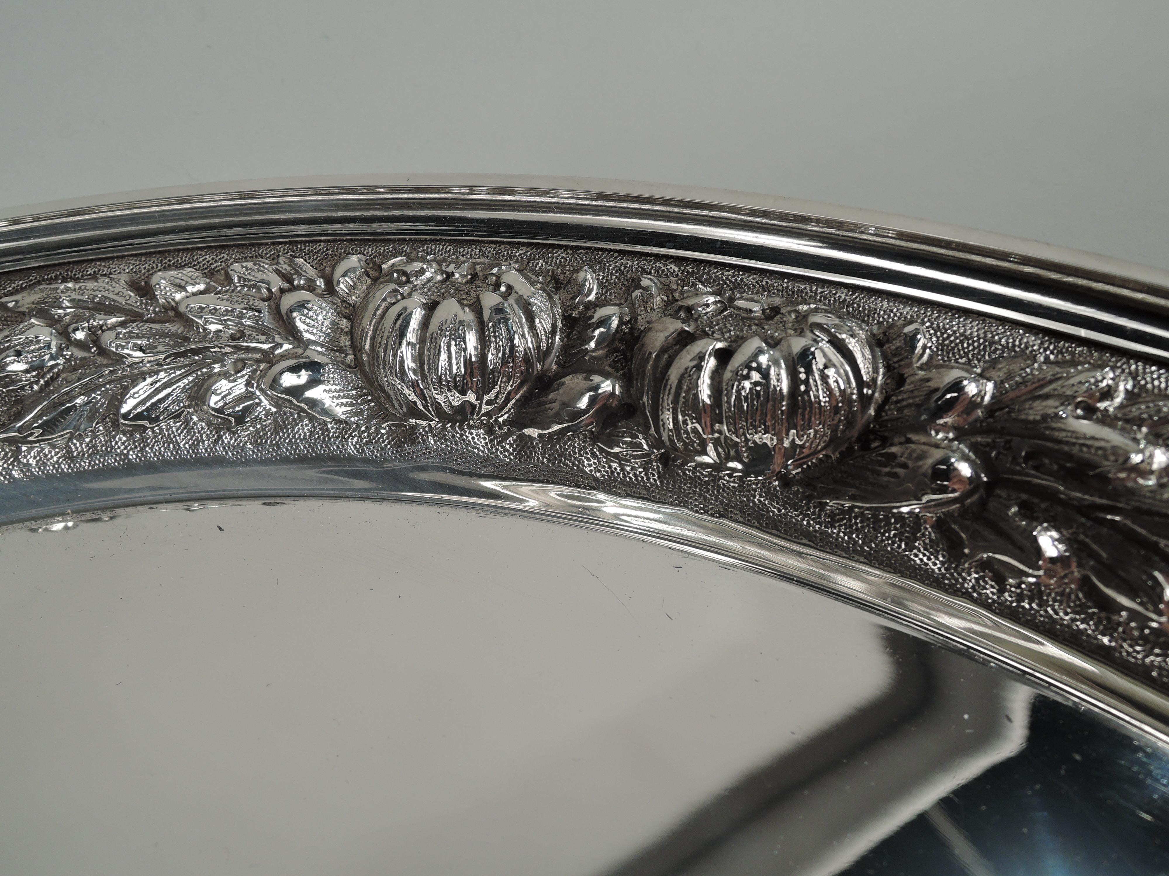Traditional sterling silver tray. Made by Stieff in Baltimore in 1956. Round and plain well and flat rim. Shoulder tapering with repousse floral garland on stippled ground. A nice piece in a regional style. Fully marked including maker’s stamp, date