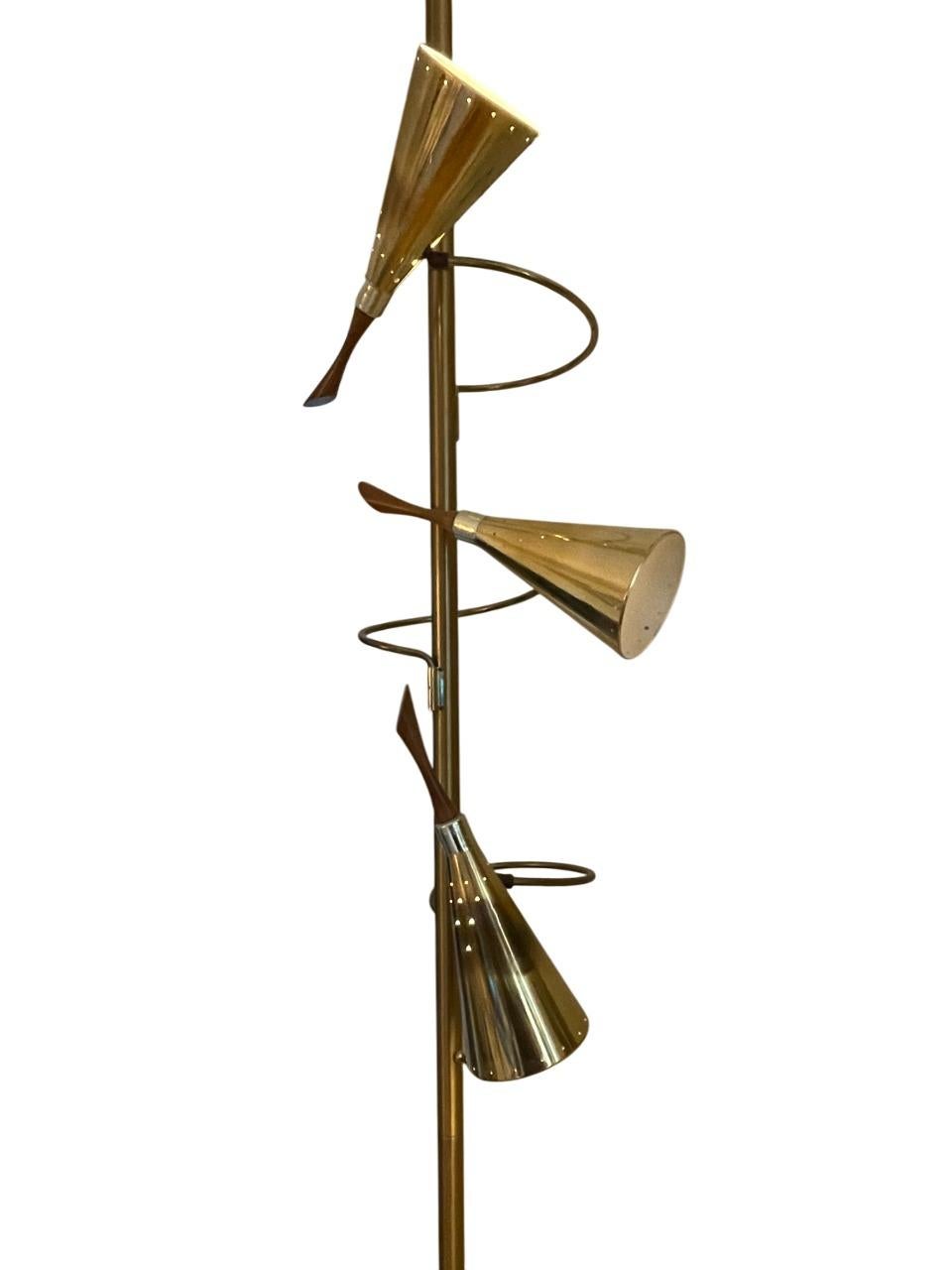 Una sofisticata lampada a palo a tensione di metà secolo attribuita a Stiffel, realizzata negli anni Cinquanta. Questo elegante pezzo presenta una struttura in ottone lucido con tre suggestivi paralumi a forma di cono disposti lungo scultorei bracci