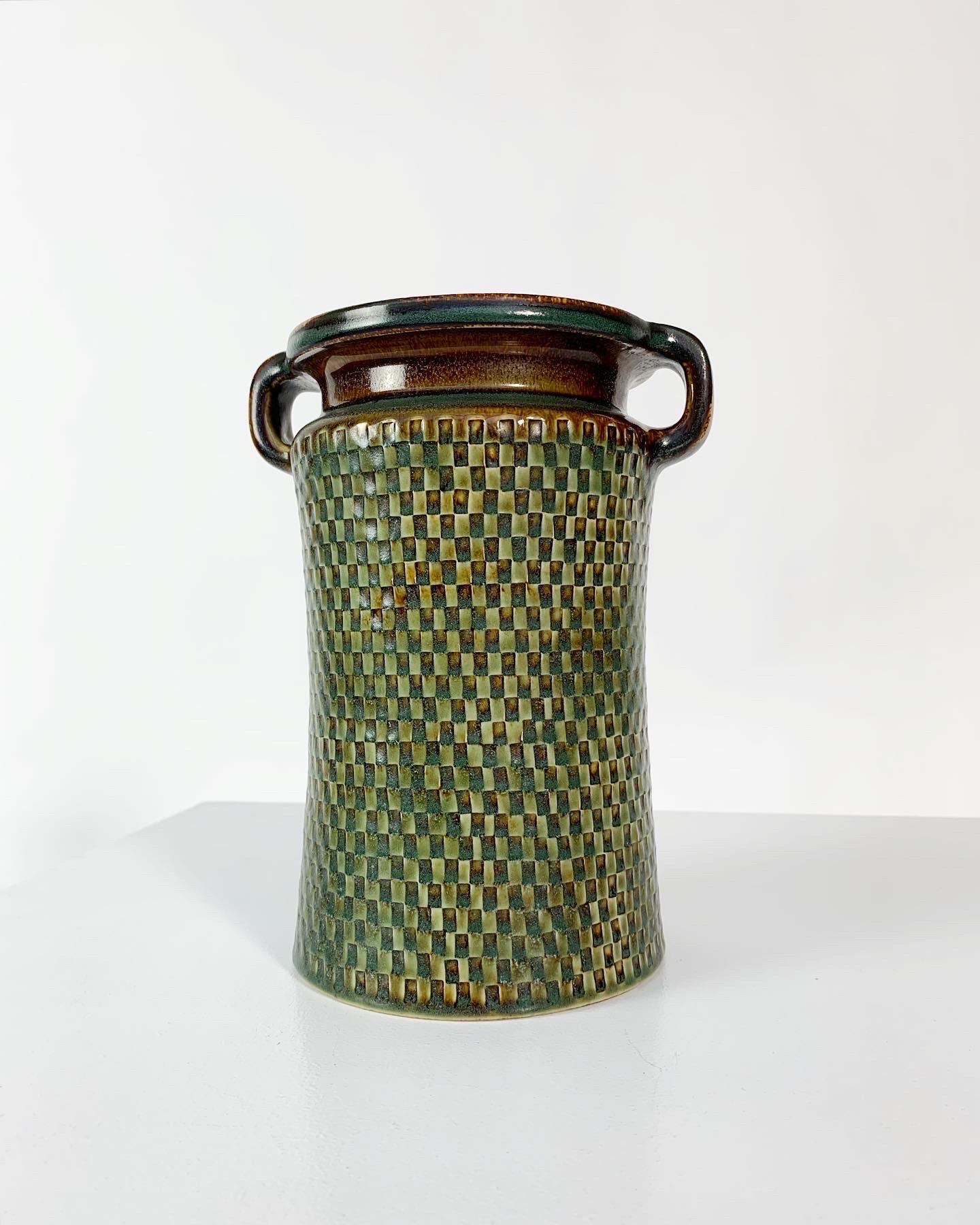 Rare stoneware vase by master caramist Stig Lindberg for the Swedish ceramic manufacturer Gustavsberg in 1968.

Beautiful relief checker pattern, glazed in hues of green and brown. Hand-signed underneath.

Measures: Height: 21 cm
Width with