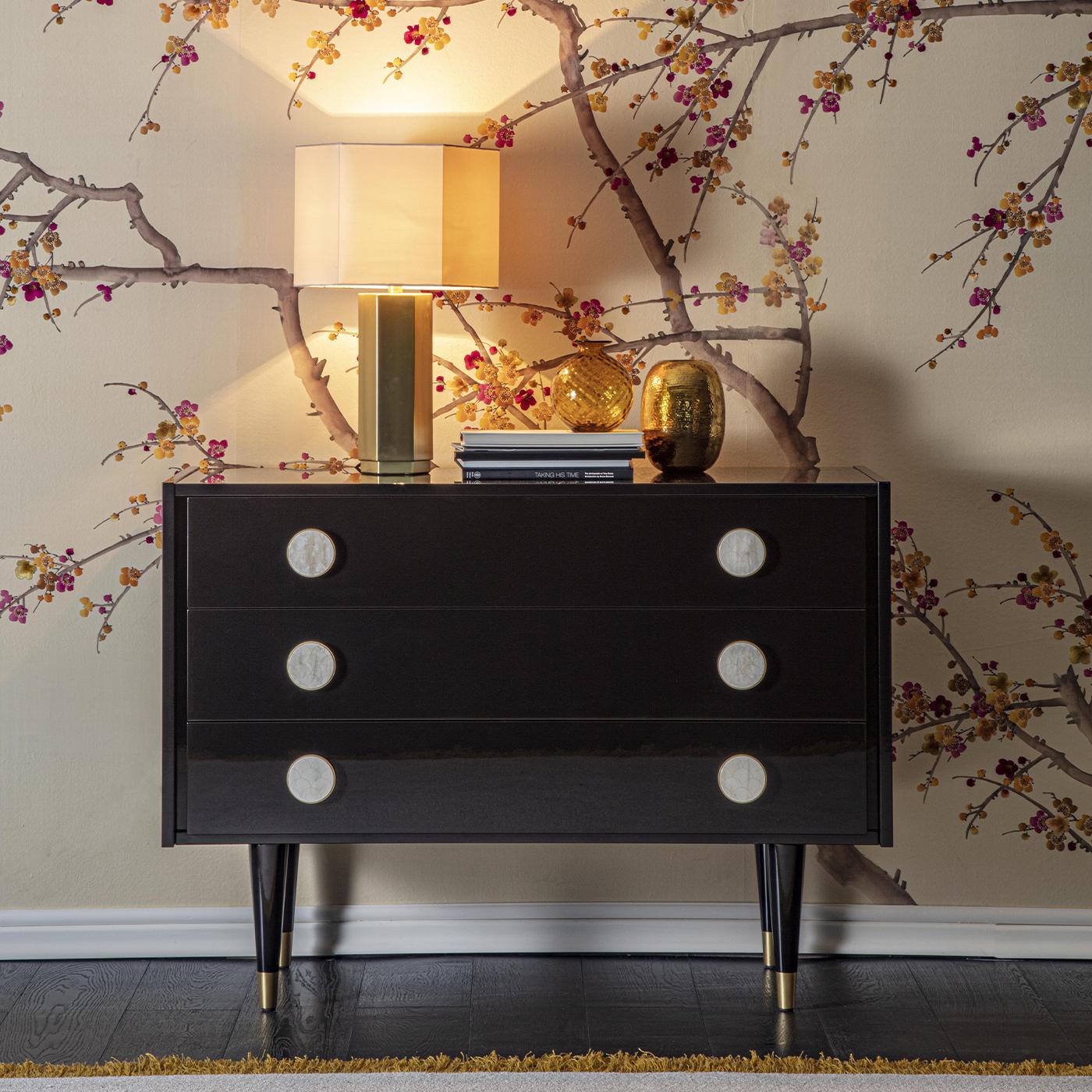 This statement-making wooden chest of drawers lacquered in glossy dark-brown exudes a bold character deriving from neat and generous volumes. Resting on tapered legs accented with satin brass feet, the storage unit is comprised of three ample