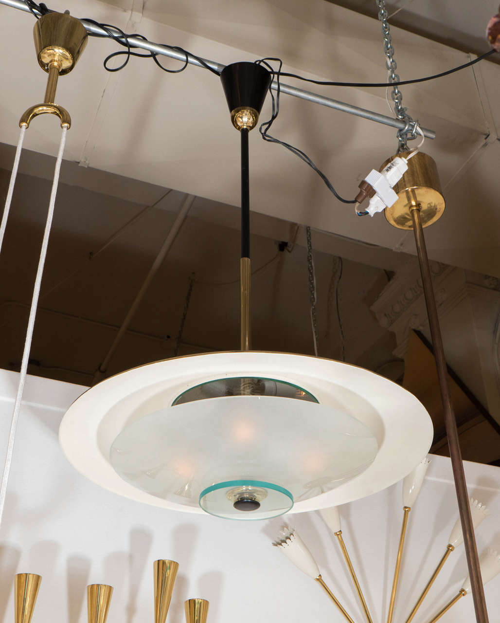 A beautifully made 1950s Italian modern design pendant light in a saucer shape attributed to the famed Italian lighting company Stilnovo. The top dish of the lamp is polished brass while the underneath is white enamel to allow the light to reflect.