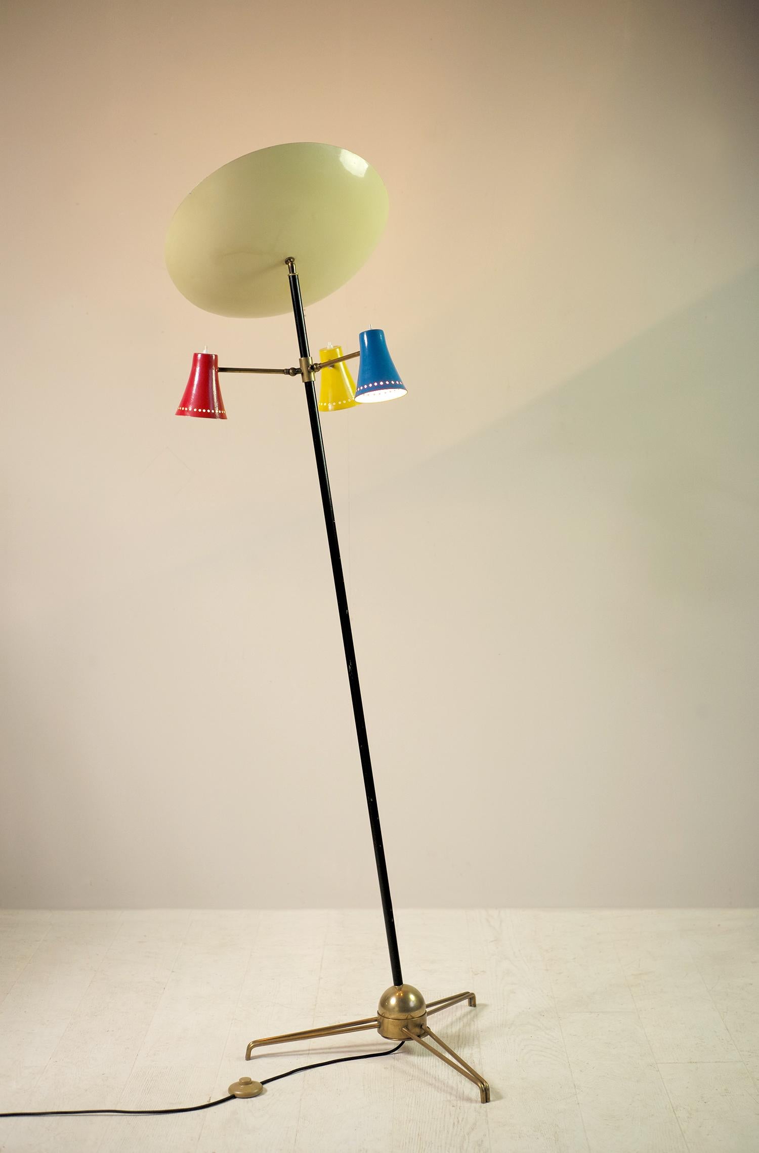 Tripod floor lamp in lacquered metal and brass, Stilnovo 1950. The black lacquered shaft rests on a heavily leaded sphere allowing the tilt to be adjusted. Three arms of lights adjustable by a ball and socket head receive polychrome blue, yellow and