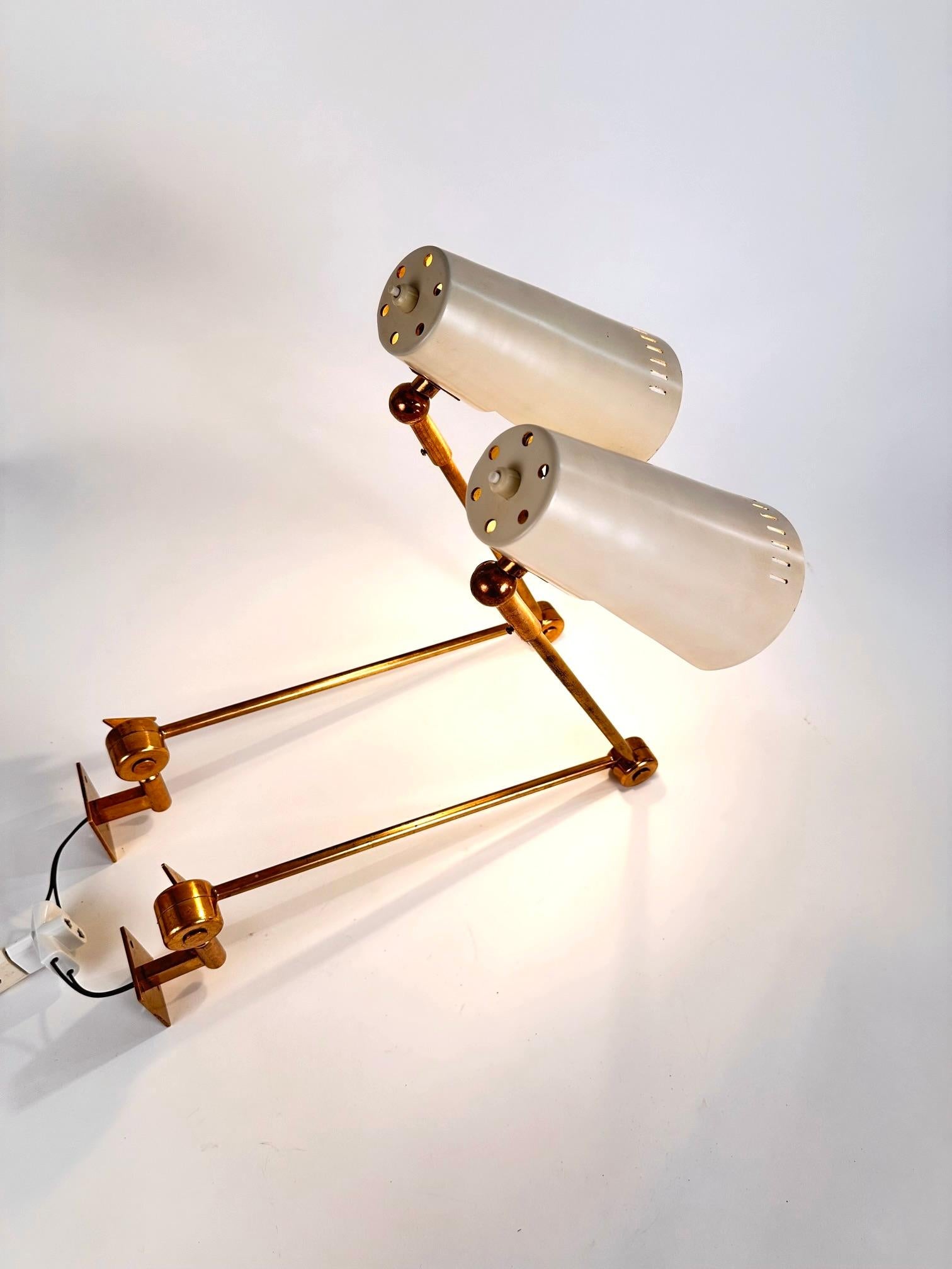 An original pair of  fully articulated original Stilnovo  wall lamps.(marked Stilnovo).. Italy 1960 .Solid brass adjustable arms ,which could rotate and adjust to several positions according to purpose.The lamps have an original white finished shade