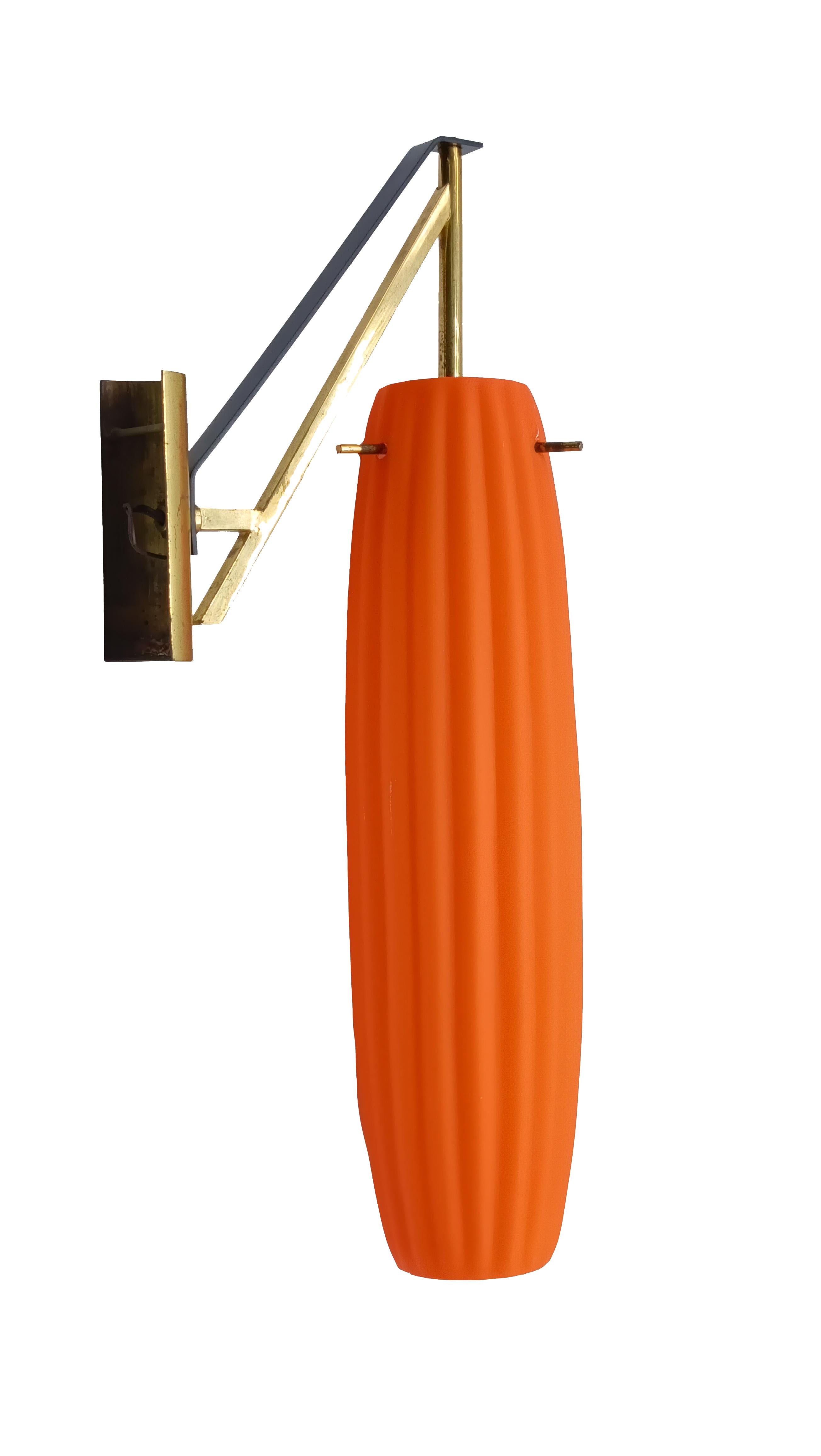 Wall lamp made of metal with black and brass finish, consists of inclined arms that support the lamp body. The diffuser is the real star: it is made of bright orange glass with an elongated, slightly tapered shape. It features a vertical ribbed