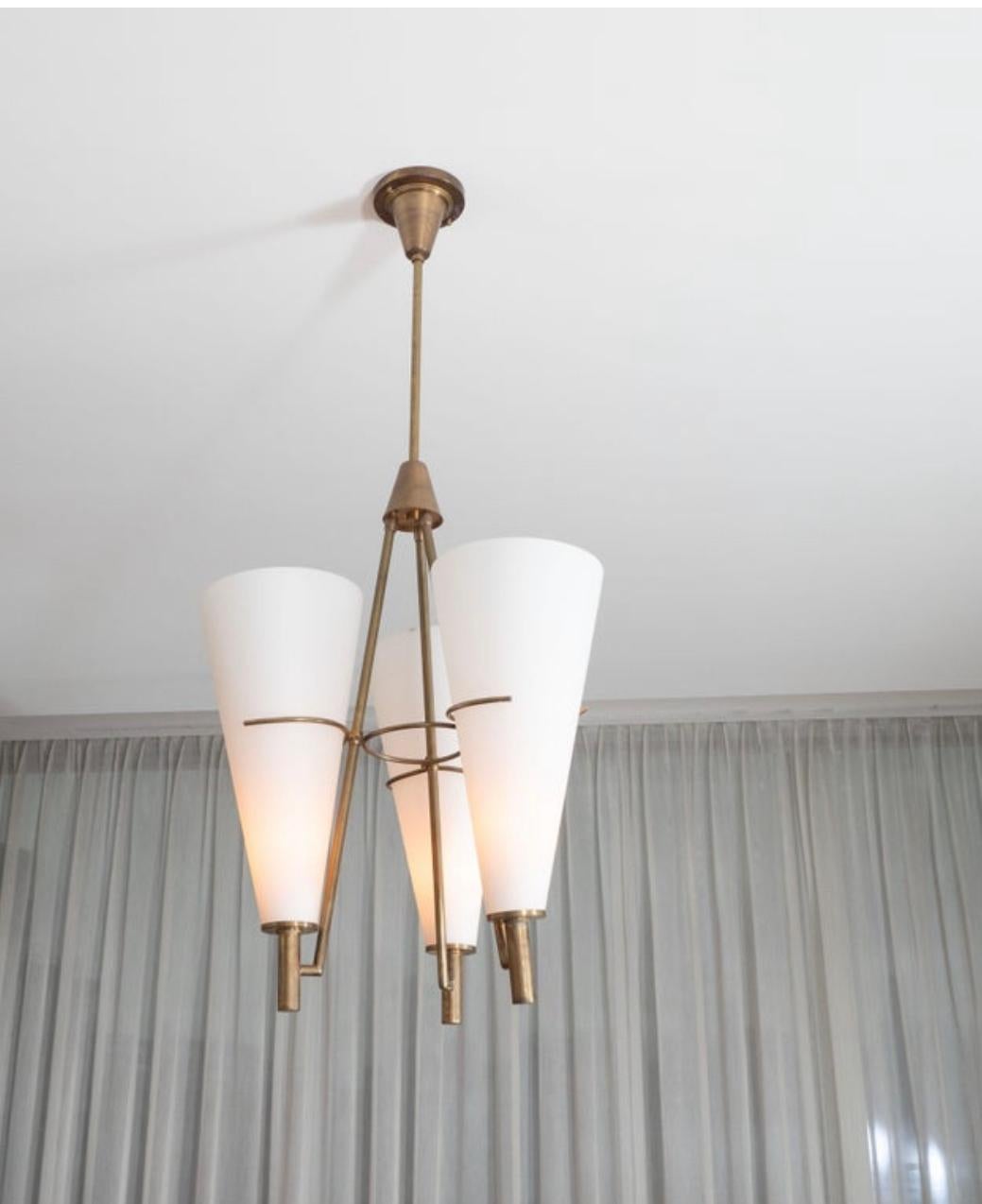 A single elegant light fixture attributed to Stilnovo. Unsigned.

Italy, circa 1960.

Light is composed of three large conical opaline glass shades, retained by delicate brass claws and resting on small high cylinders. The three gilt brass arms join