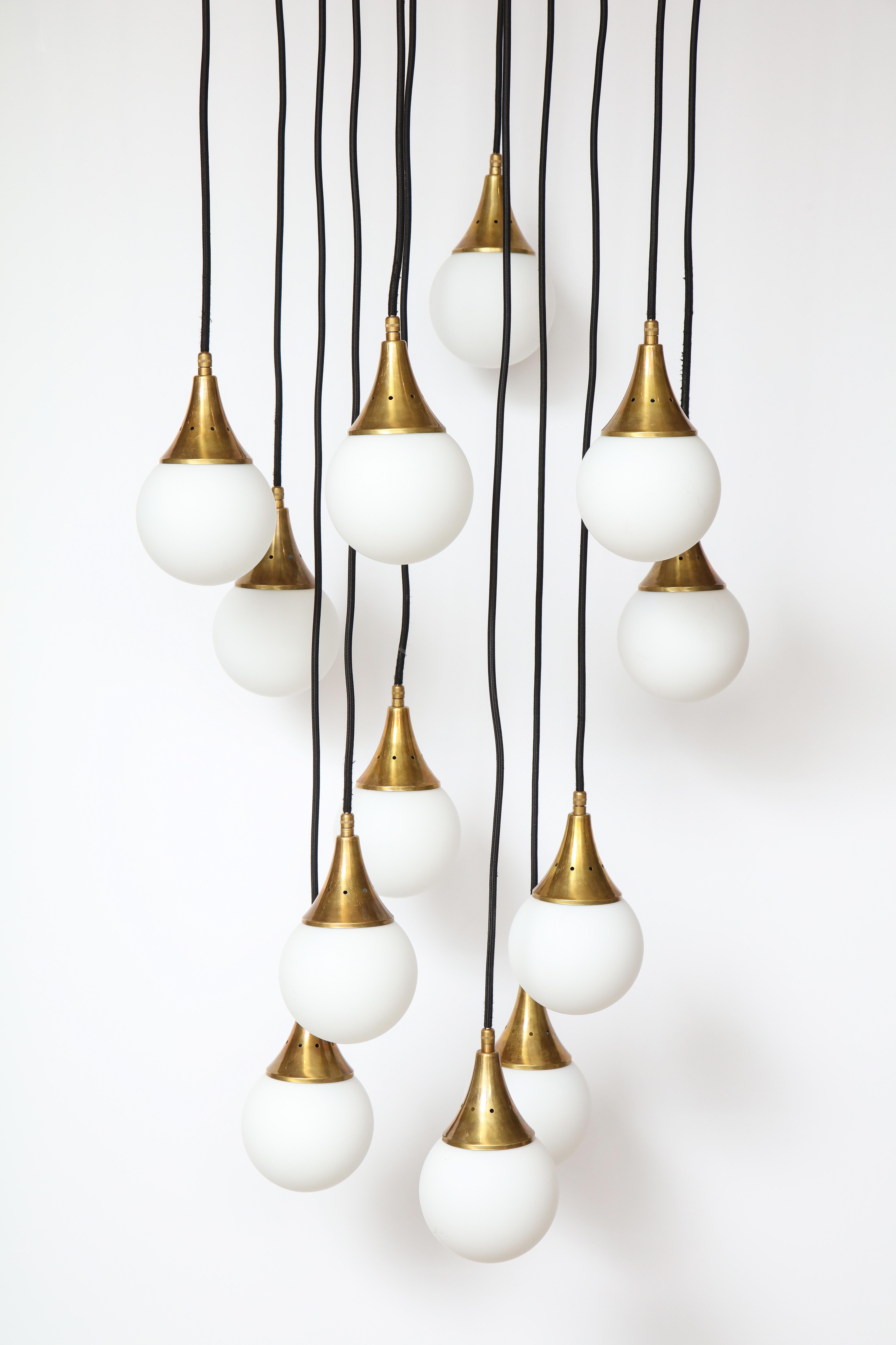 Stilnovo cascading chandelier with twelve opaline glass ball lights supported by brass canopies and suspended by adjustable black fabric wiring. The glass lighting can be adjusted via the fabric wiring to various height levels. The whole supported