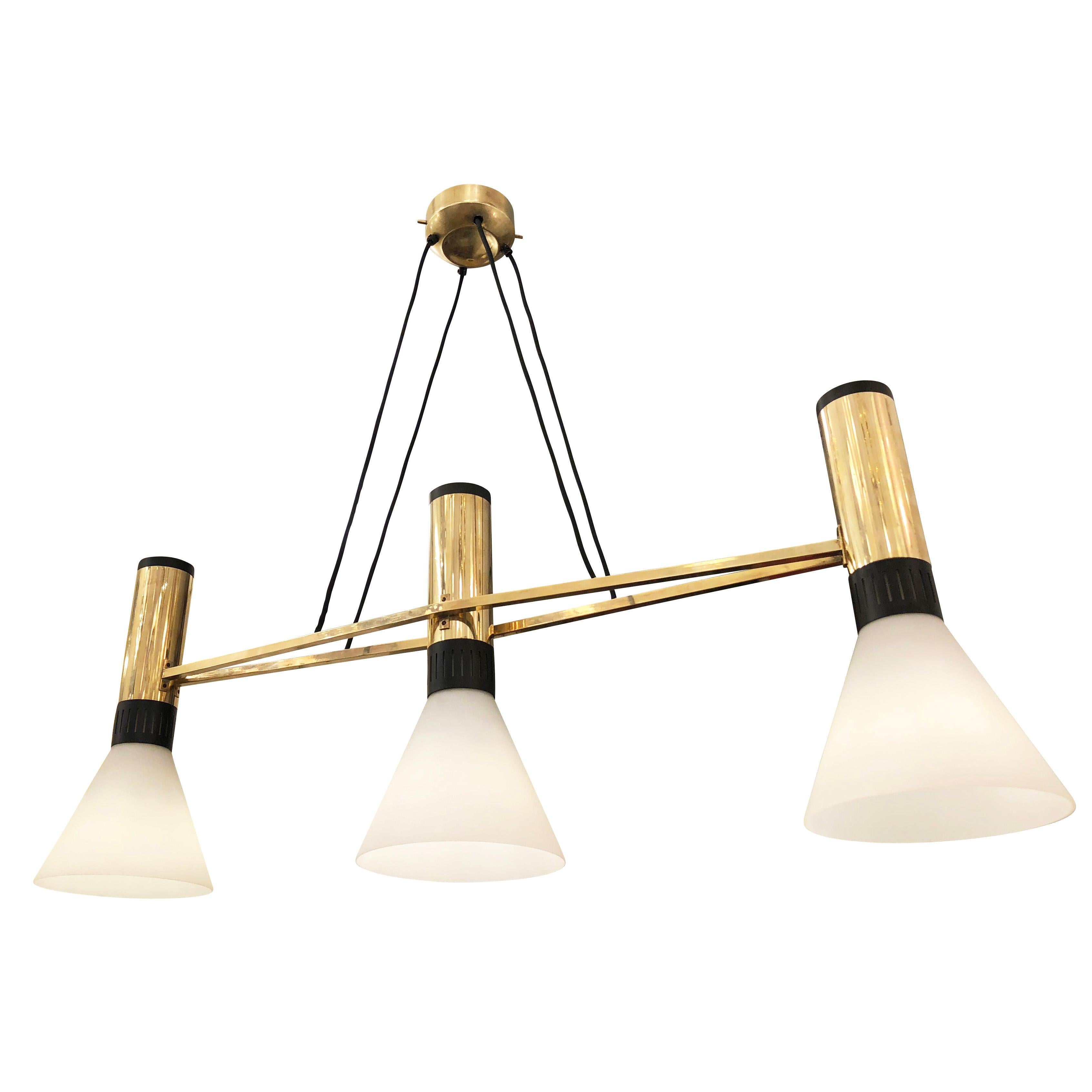 Elongated Stilnovo chandelier with three conical glass shades on a brass frame. Ideal over a dining table. Height is adjustable via the four fabric cords. Holds three E26 bulbs. Original label still present.

Condition: Excellent vintage