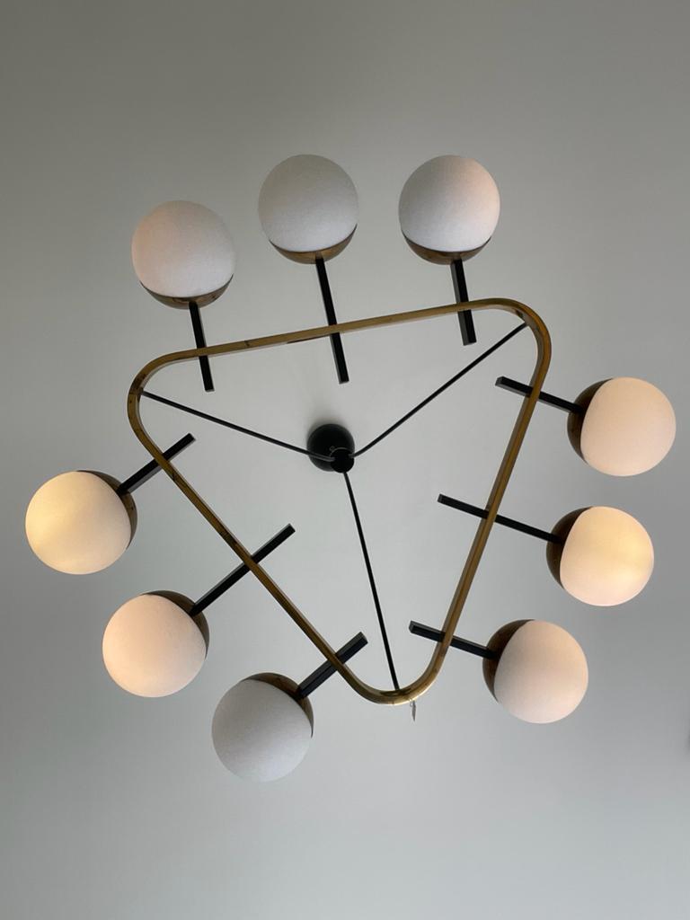 Chandelier manufactured by Stilnovo in Italy, 1960s.
A brass chandelier that immediately stands out for its triangular shape from which black small bars emerge and hold the nine spherical-shaped diffusers of white opal glass.
The bars are three on