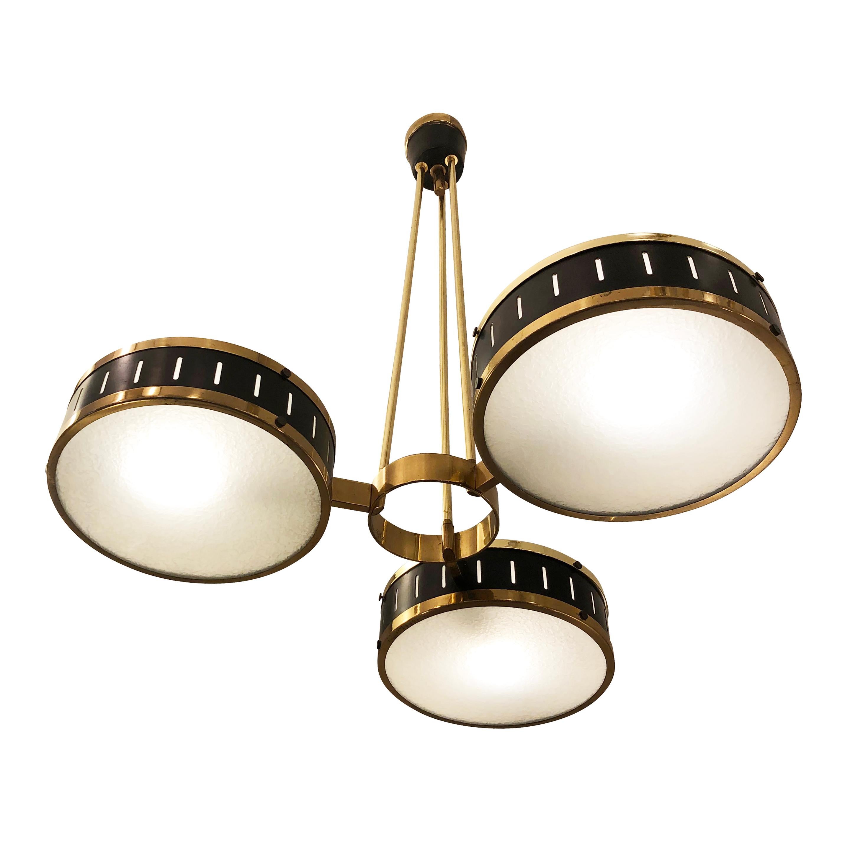 Elegant Mid-Century chandelier by Stilnovo with three “drum” like shades; each one is lacquered black with brass rims and has textured frosted glass on both sides. The three brass stems converge in a single canopy. Holds three candelabra