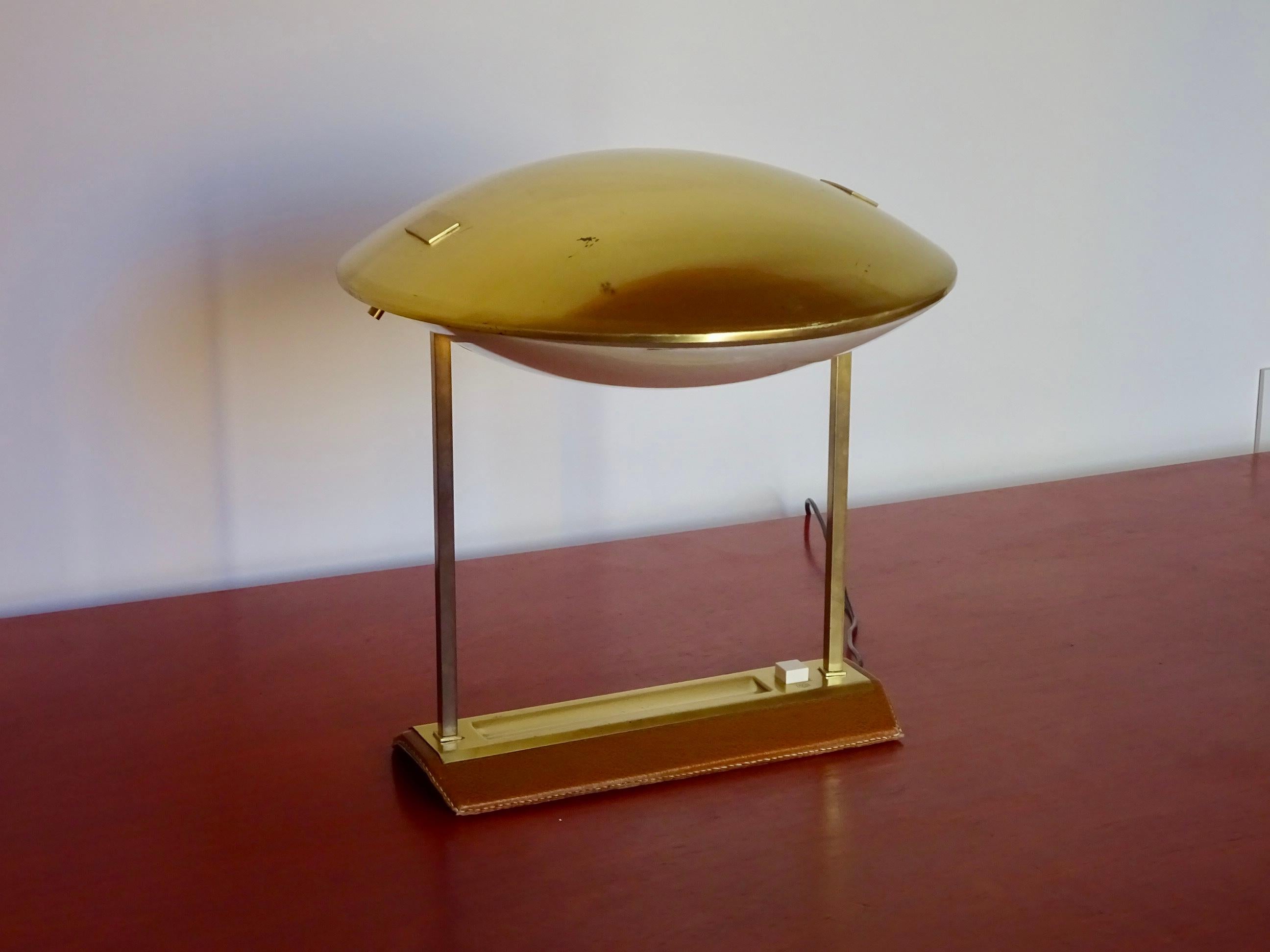 Lampe de table à orientation réglable. Modèle 8050 conçu par Stilnovo au début des années 60 et également produit par Metalarte. Avec une base rectangulaire en cuir brun et une structure métallique dorée qui forme un porche supportant un dôme