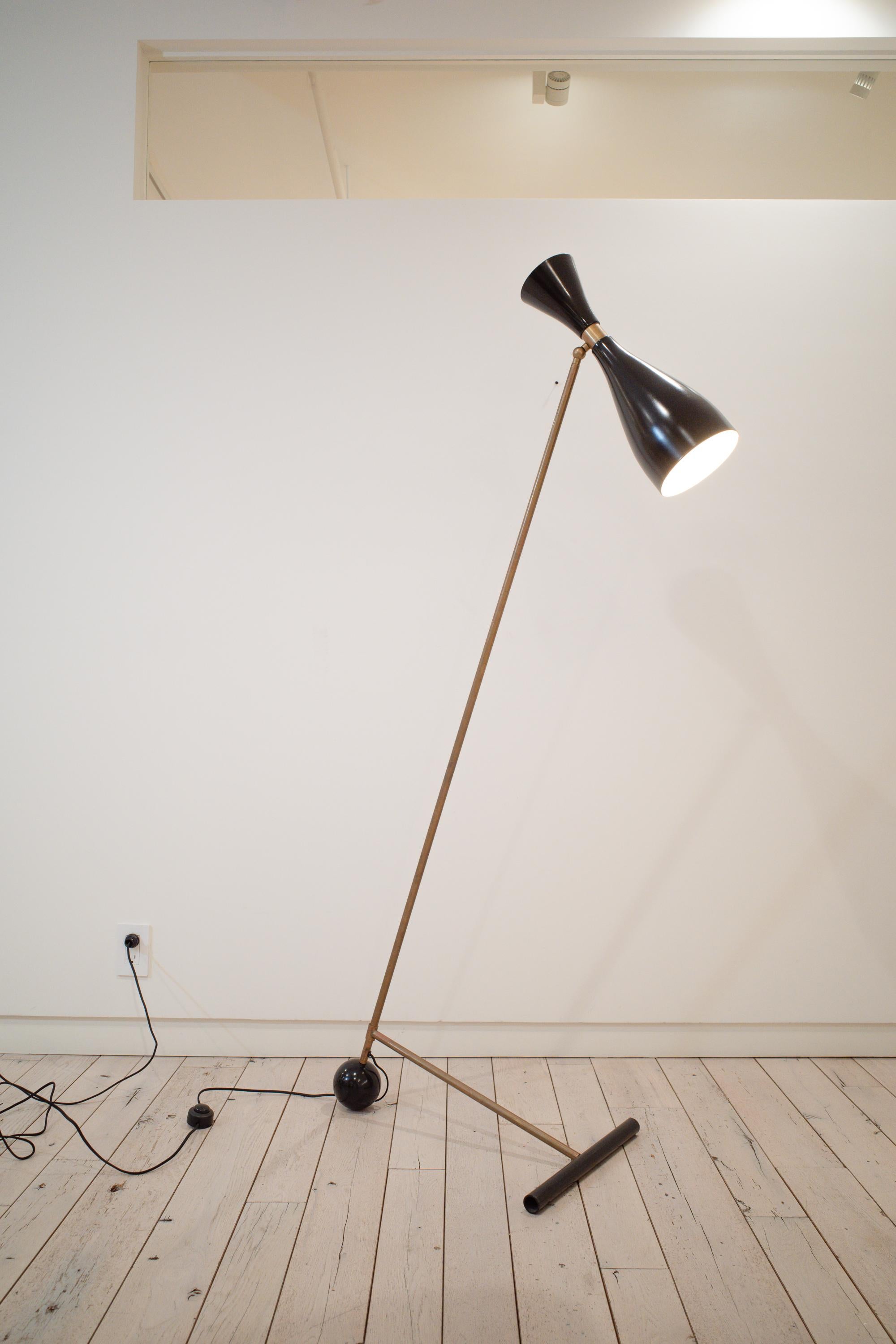 Ce lampadaire sophistiqué de style Mid-Century Modern présente un design dynamique et hautement fonctionnel construit autour d'un contraste de matériaux saisissant. Le luminaire utilise un abat-jour articulé en métal noir, permettant de diriger la