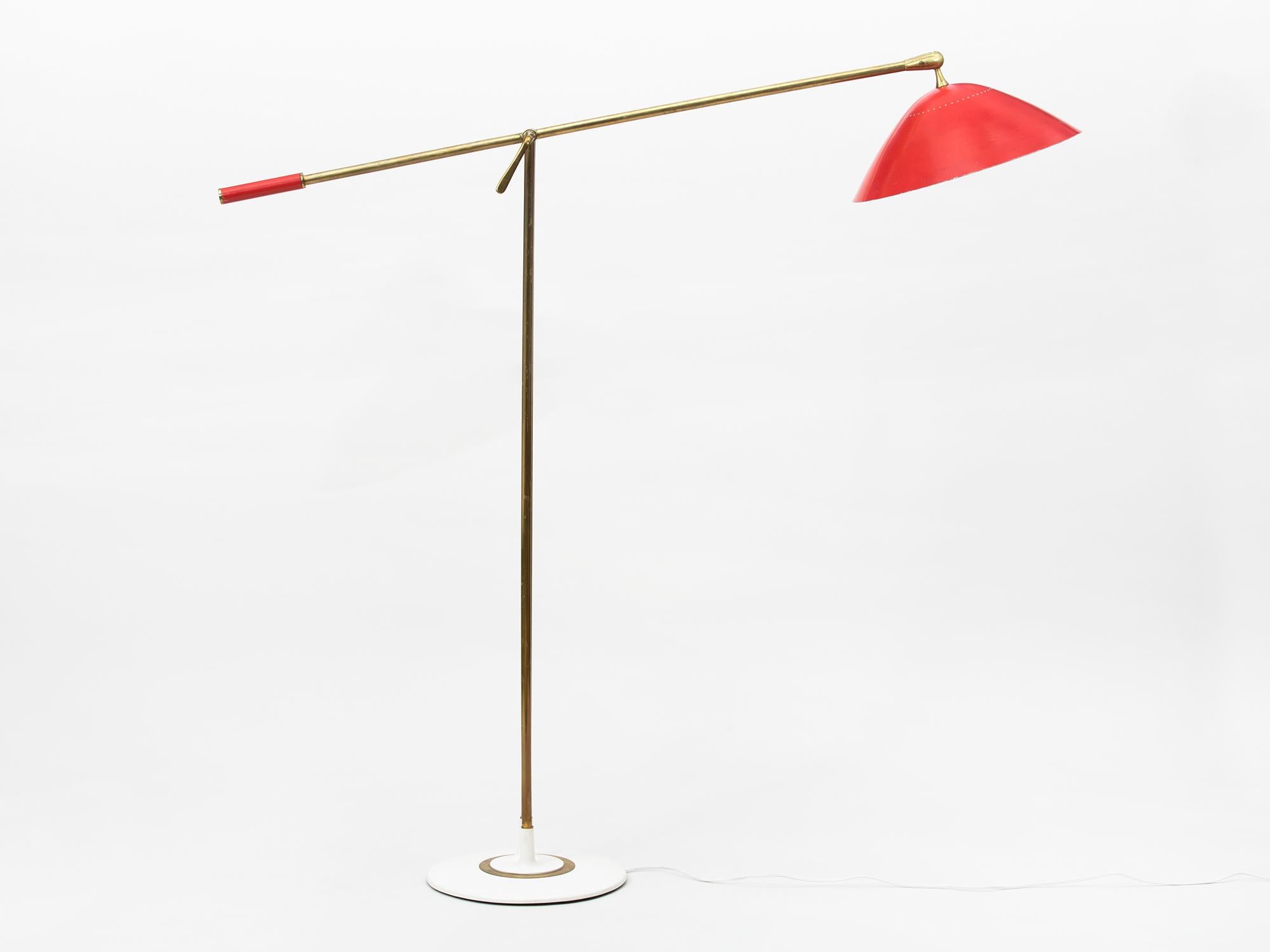 Elegant, adjustable midcentury brass floor lamp with bright red lacquered perforated metal shade and handle. The body of the lamp features beautifully rendered solid brass parts and twin brass stems. Manufactured in Milan in the 1950s by Italian