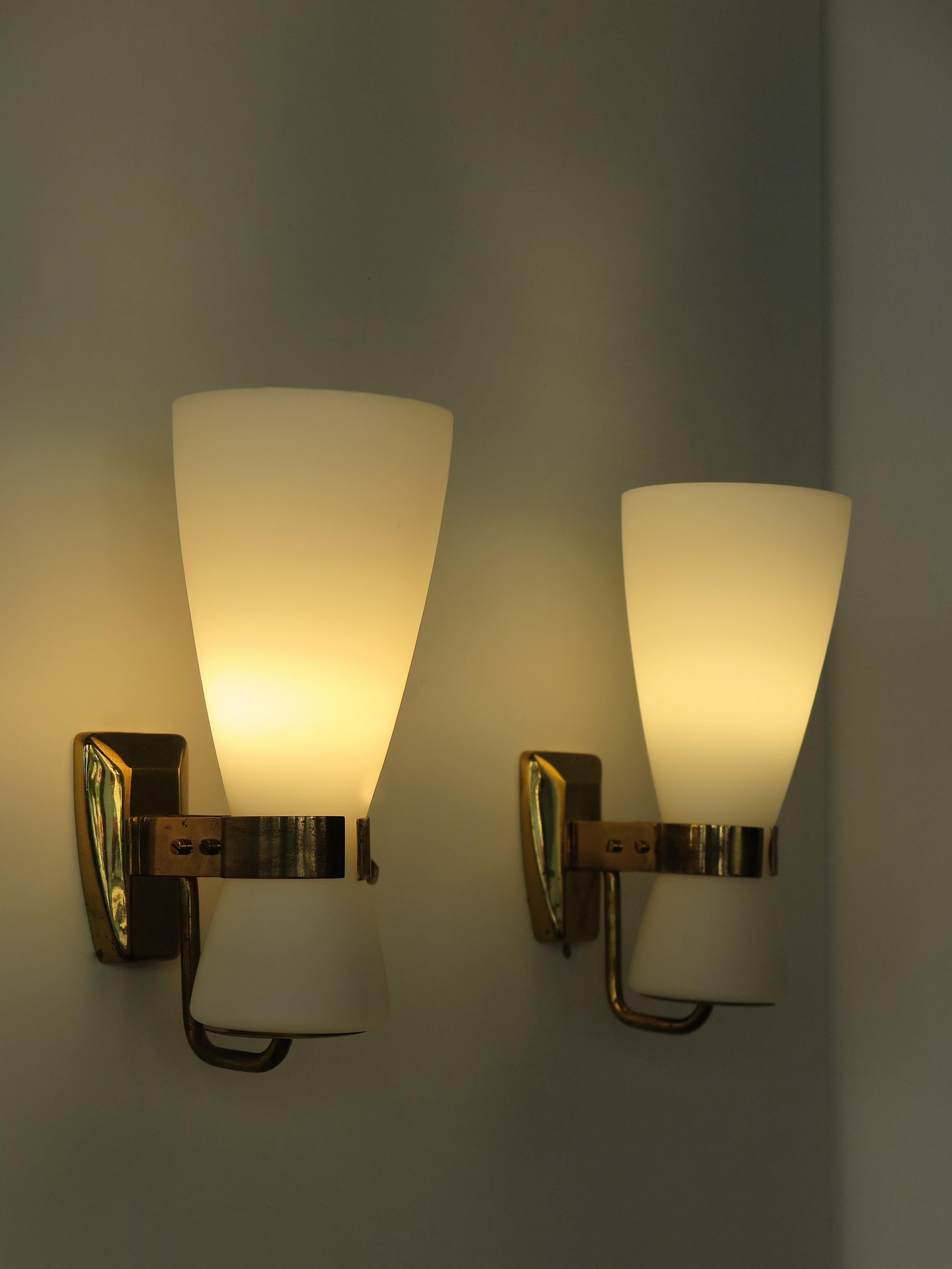 Italian midcentury modern design couple of sconces wall lamps produced by Stilnovo with white frosted glass diffusers and brass frame, 1950s Italy production Stilnovo marks engraved on frame and manufacturer’s adhesive label. 

Please note that the