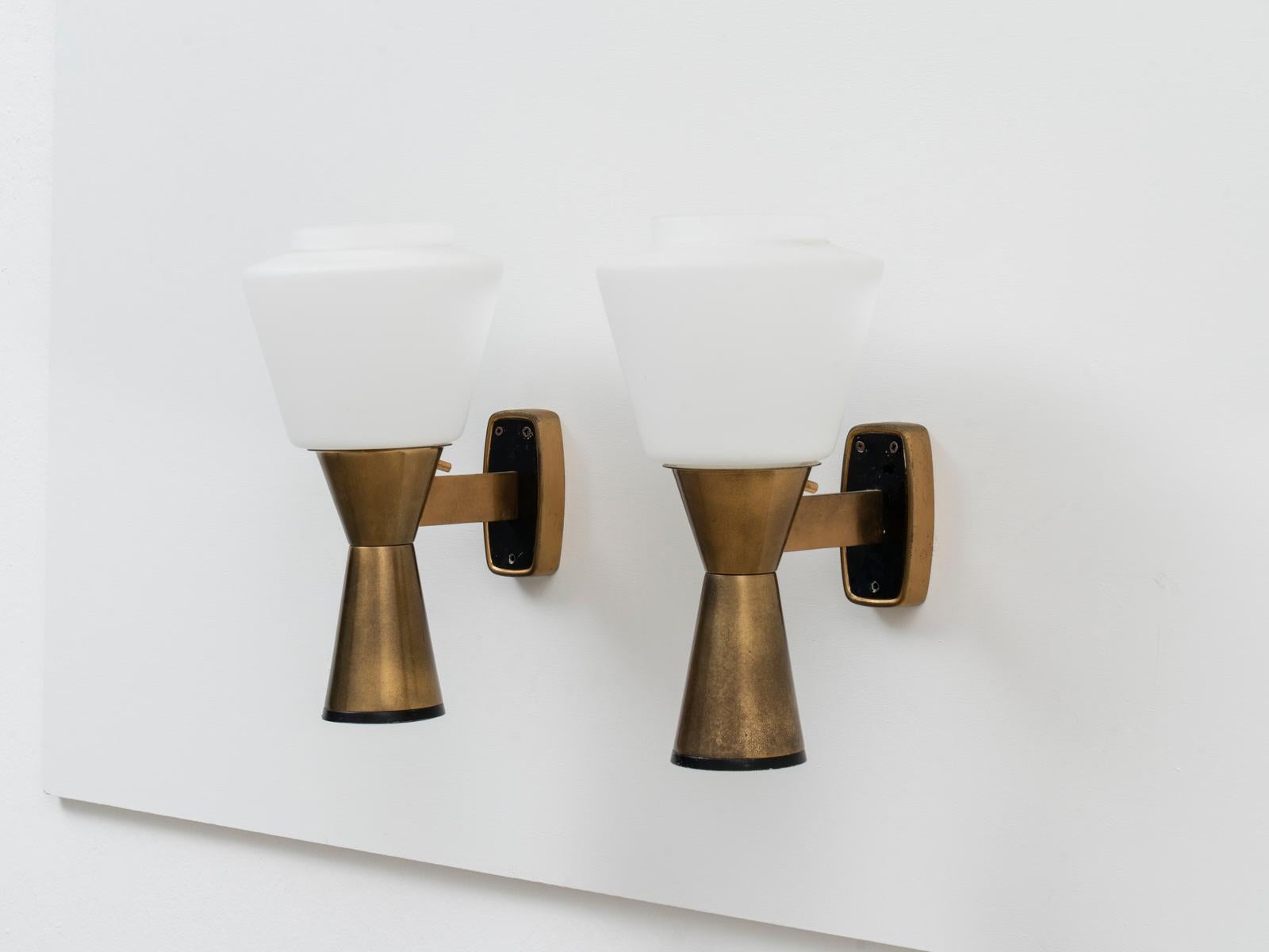 This pair of wall sconces was manufactured by Stilnovo in circa 1960. They are made of a brass structure with opaline glass diffusers. 
Both lamps are stamped 