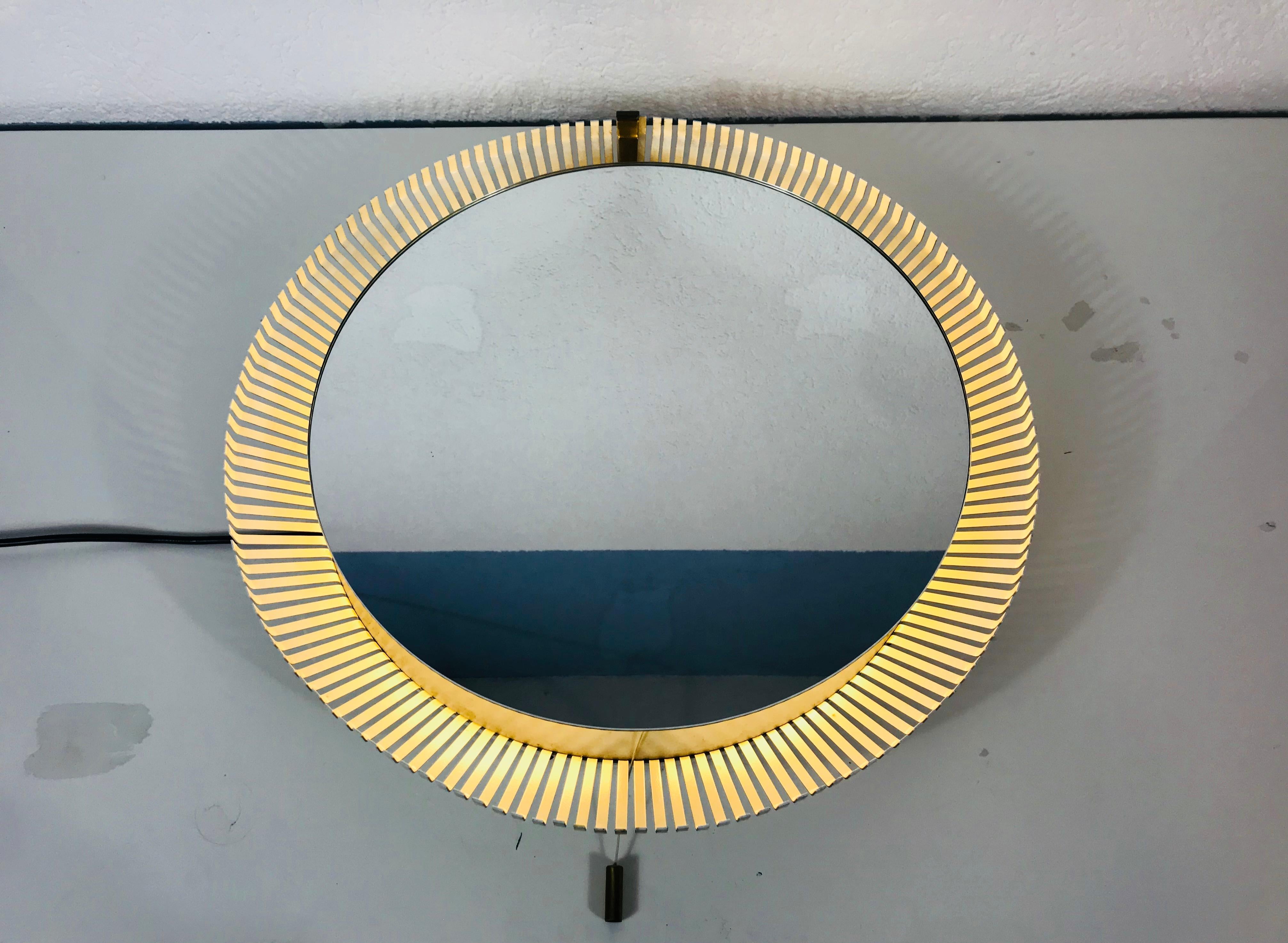 An Stilnovo illuminated wall mirror from the 1960s made in Italy. The mirror has a circular metal design. There are E14 light bulbs inside the frame. The mirror is in a good vintage condition.