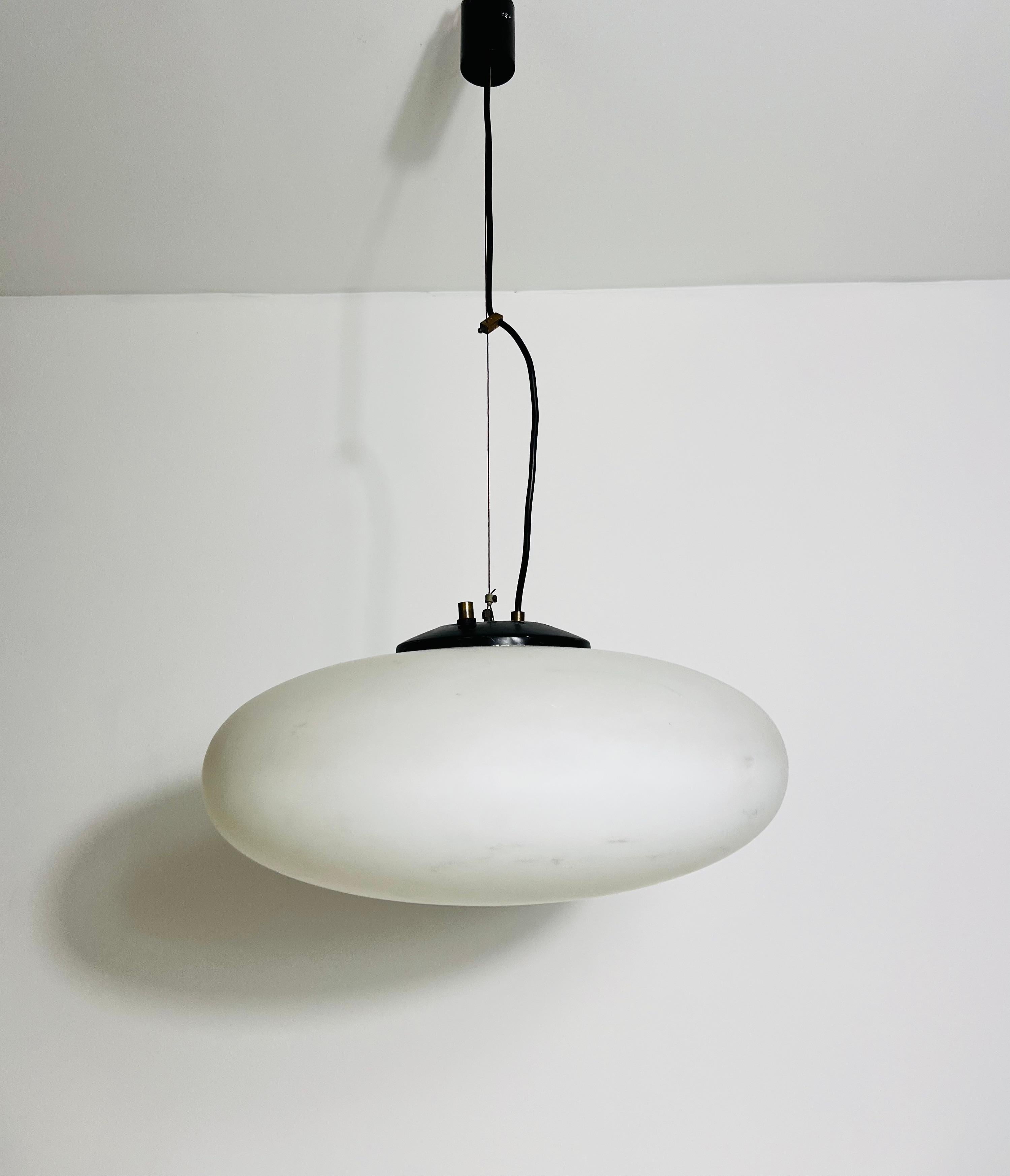 This mid-century modern ceiling lamp from the renowned Italian manufacturer Stinero, dating back to the 1950s, is a masterpiece of timeless elegance. The lamp features an oval-shaped opal glass shade, which emits a warm and inviting light, perfect