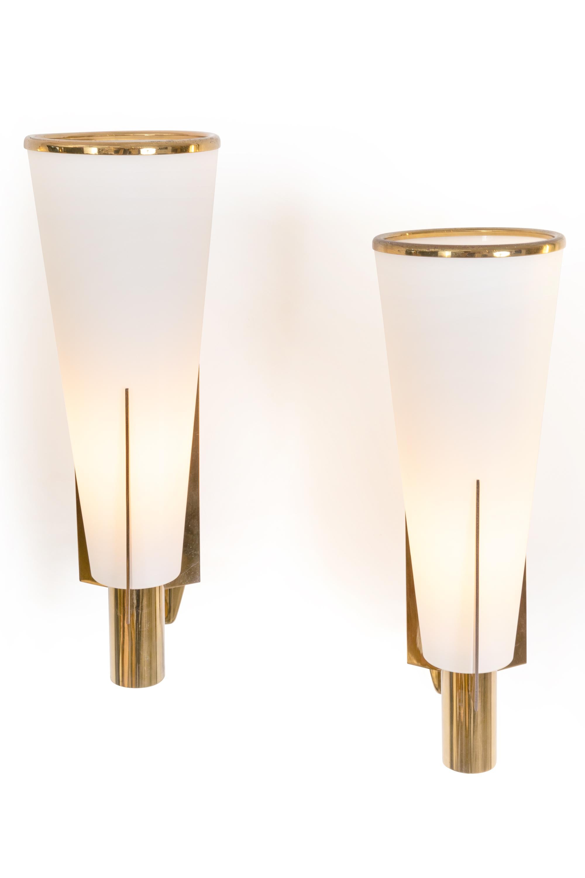 A simply elegant design and an impressive scale make these sconces a rare find. In original condition including the brass ring at the top of the tapered glass shade. Two pair are available.
