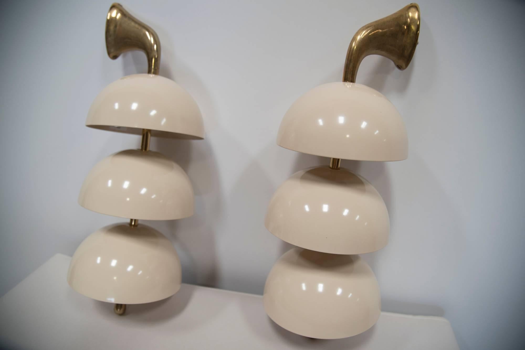 One set [making ONE PAIR] of three-light wall sconces from Stilnovo, Italy. Solid brass and cream-colored lacquer on tole. Three deep round dishes hold and hide the light are mounted on a shaped solid brass upturned, tapering arm finishing into a
