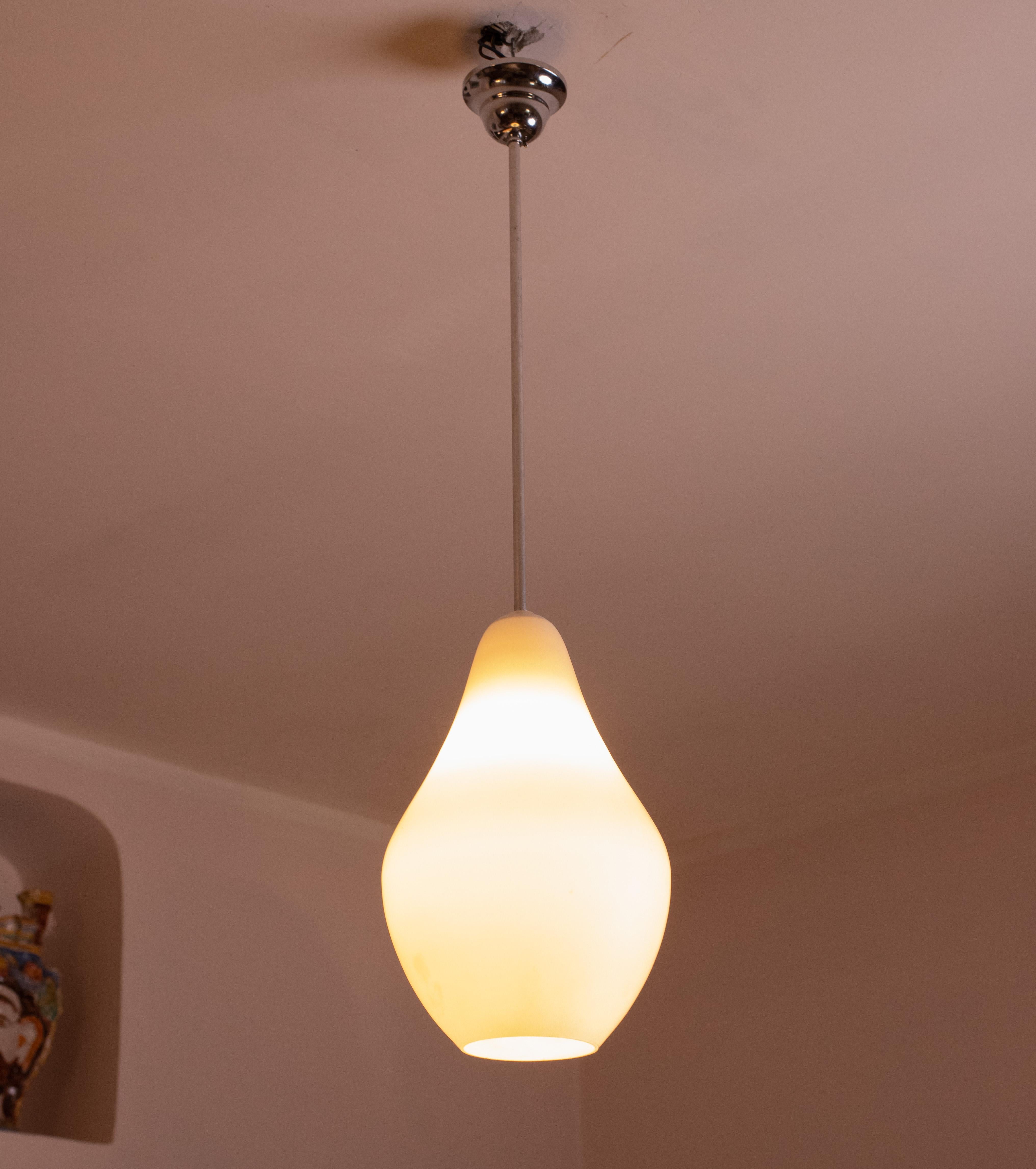 Stilnovo design opal glass pendant made in the 1970s.
 It connects to the ceiling with a brass element; the wire cover rosette has been replaced.
The pear-shaped cap is made of white opaline glass, attached to the structure by an aluminum element.