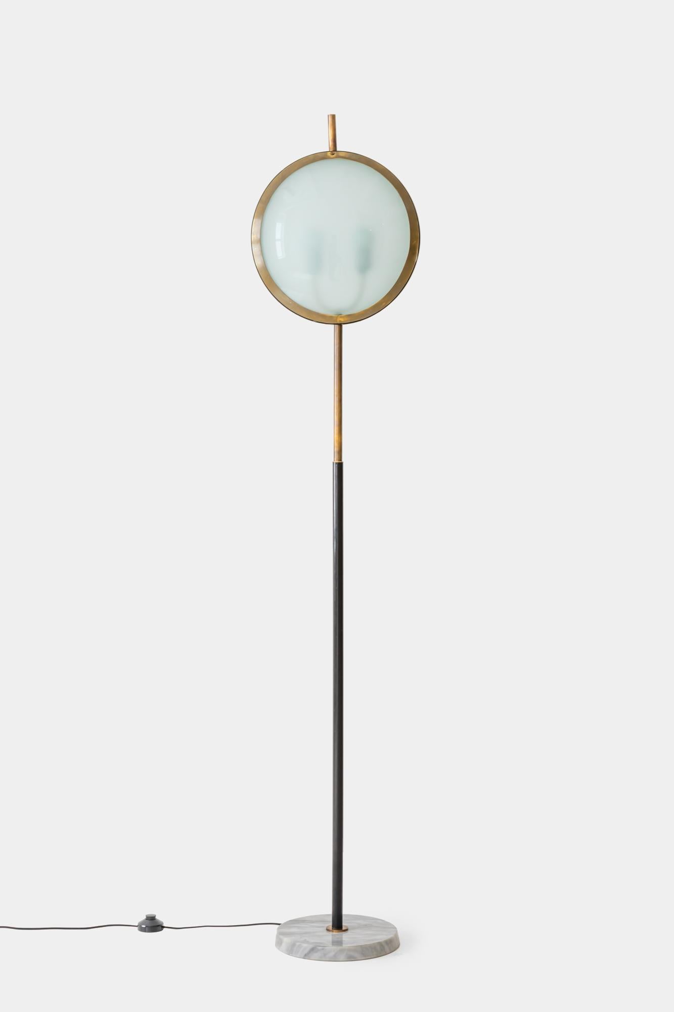 Stilnovo very rare floor lamp with convex textured glass shades on each side of brass and lacquered metal circular frame with brass finial, suspended on brass and black enameled stem on circular white marble base, Italy, 1950s. This original and