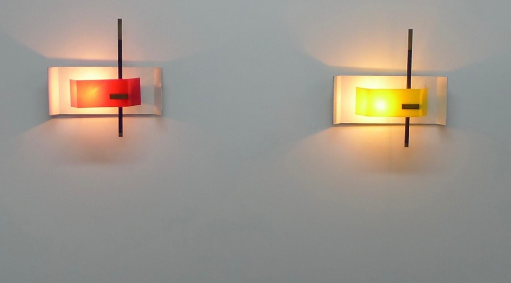 These two Stilnovo wall lights appear to be a variation of model 2020 designed by Bruno Gatta in 1955.

Each plexiglass diffuser, one yellow and one red, is decorated with a brass plaque and is moveable to allow replacement of the bulb.  The light