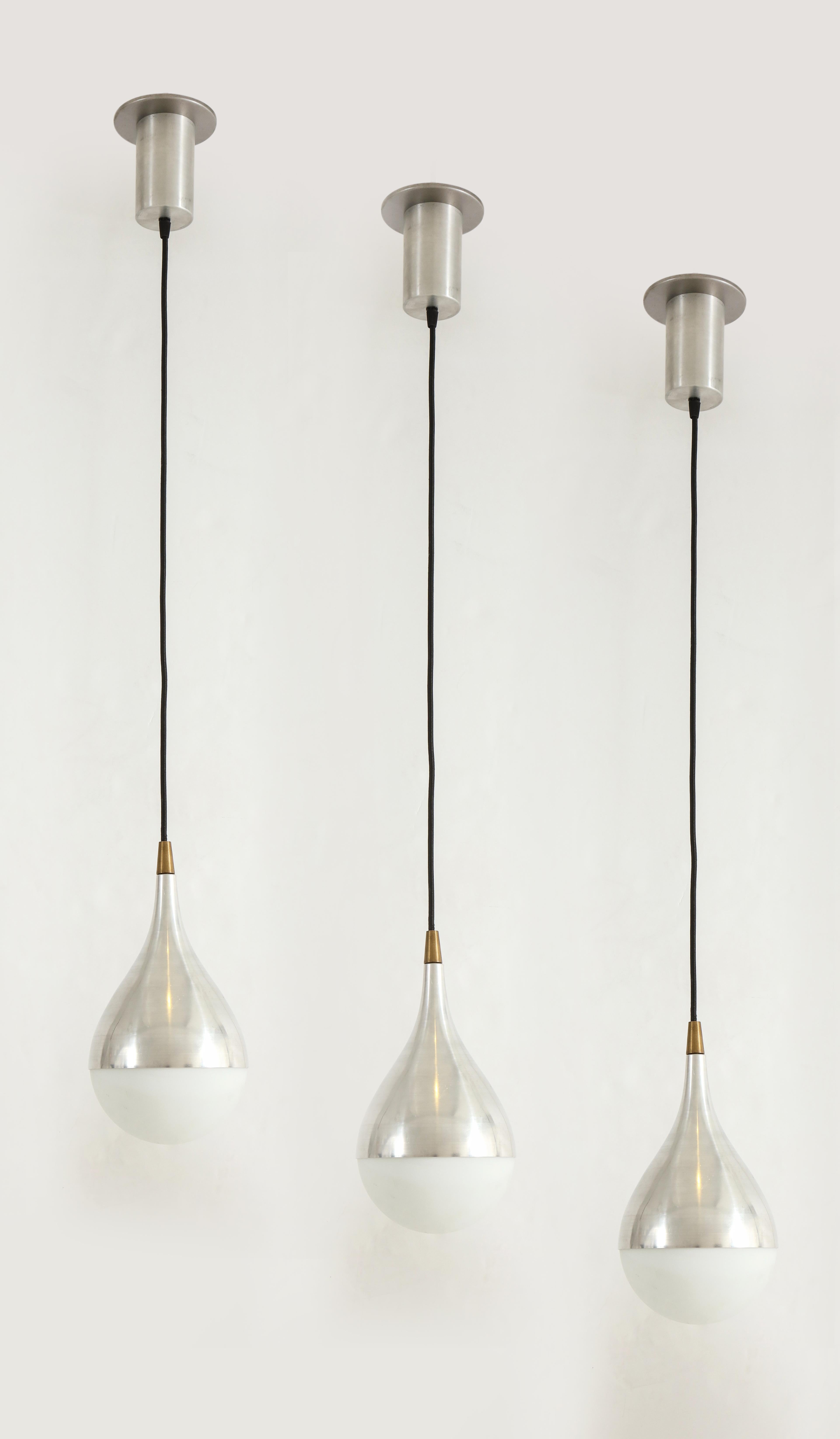 Set of three rare pendants each with opaline glass globe shades held by brushed aluminum and brass fittings suspended by cable and original brushed aluminum canopy. This iconic Stilnovo model displays an elegantly simple teardrop shape.  Its
