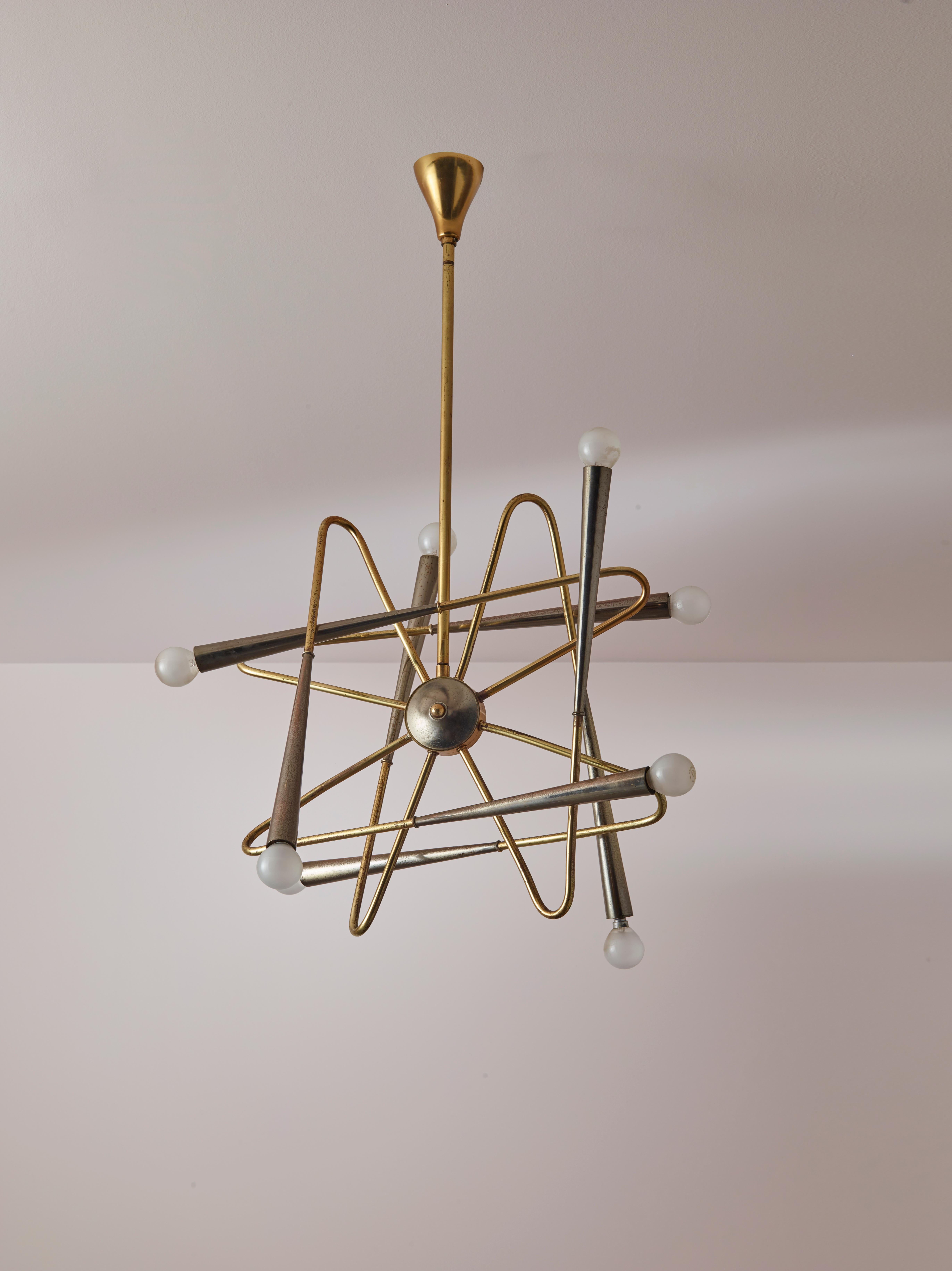 A sputnik chandelier from the 1960s, manufactured in Italy by the renowned manufacturer Stilnovo. This rare lighting fixture features a central burnished brass medallion held in place by a rigid brass rod. Its design is characterised by six curved