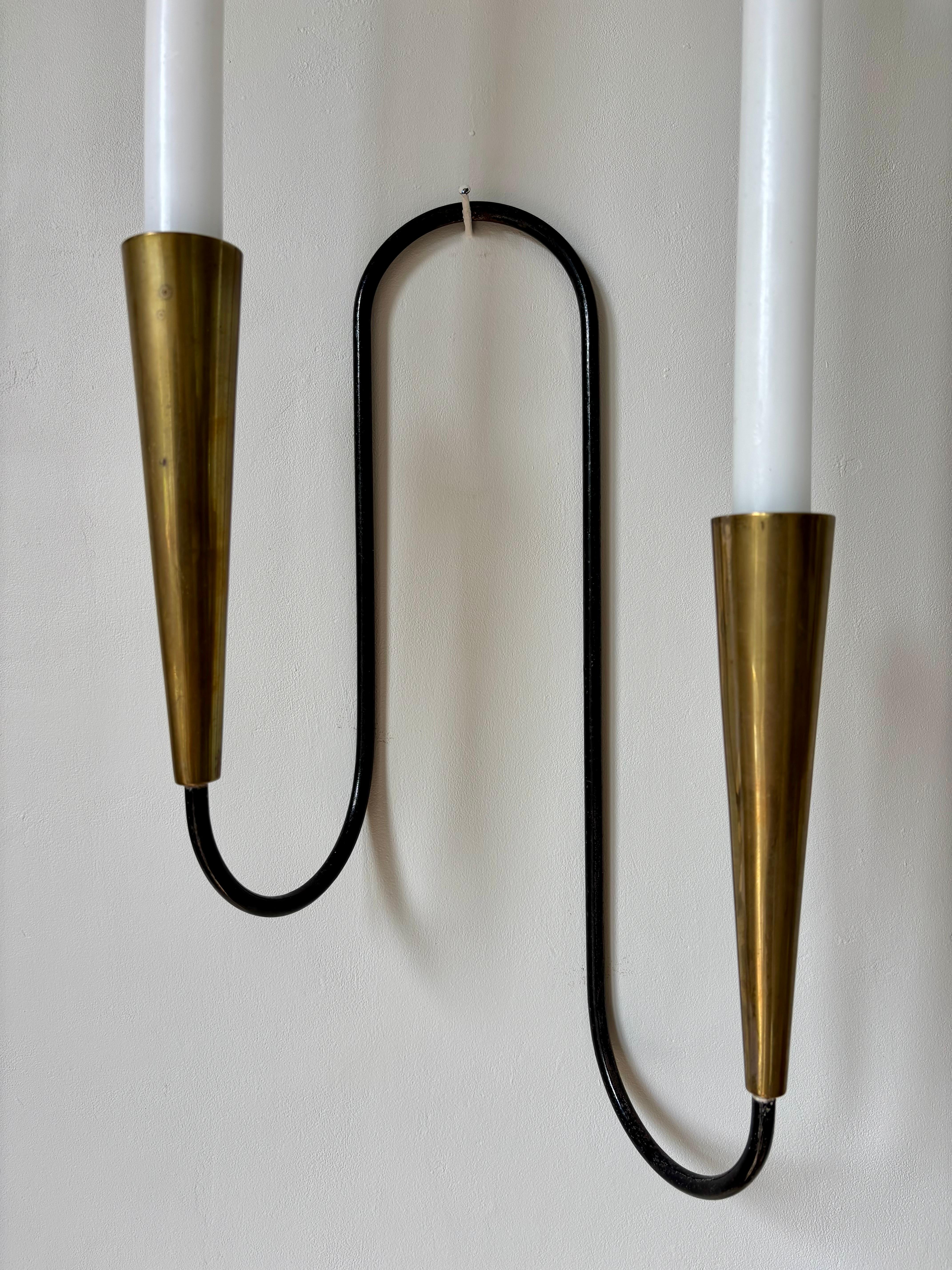 Portacandele da parete semplicistico in metallo nero e ottone per due candele di dimensioni standard. Snella montatura nera con supporti in ottone a forma di cono. Probabilmente prodotto negli anni '40 nello stile di Stilnovo e Bauhaus. 
Bellissime